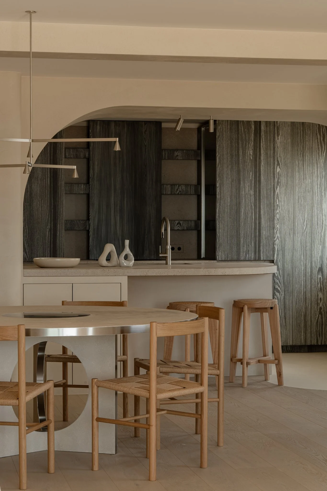 Minimalist kitchen with wooden bar stools, a round dining table with a built-in cooktop, and dark wood cabinets.