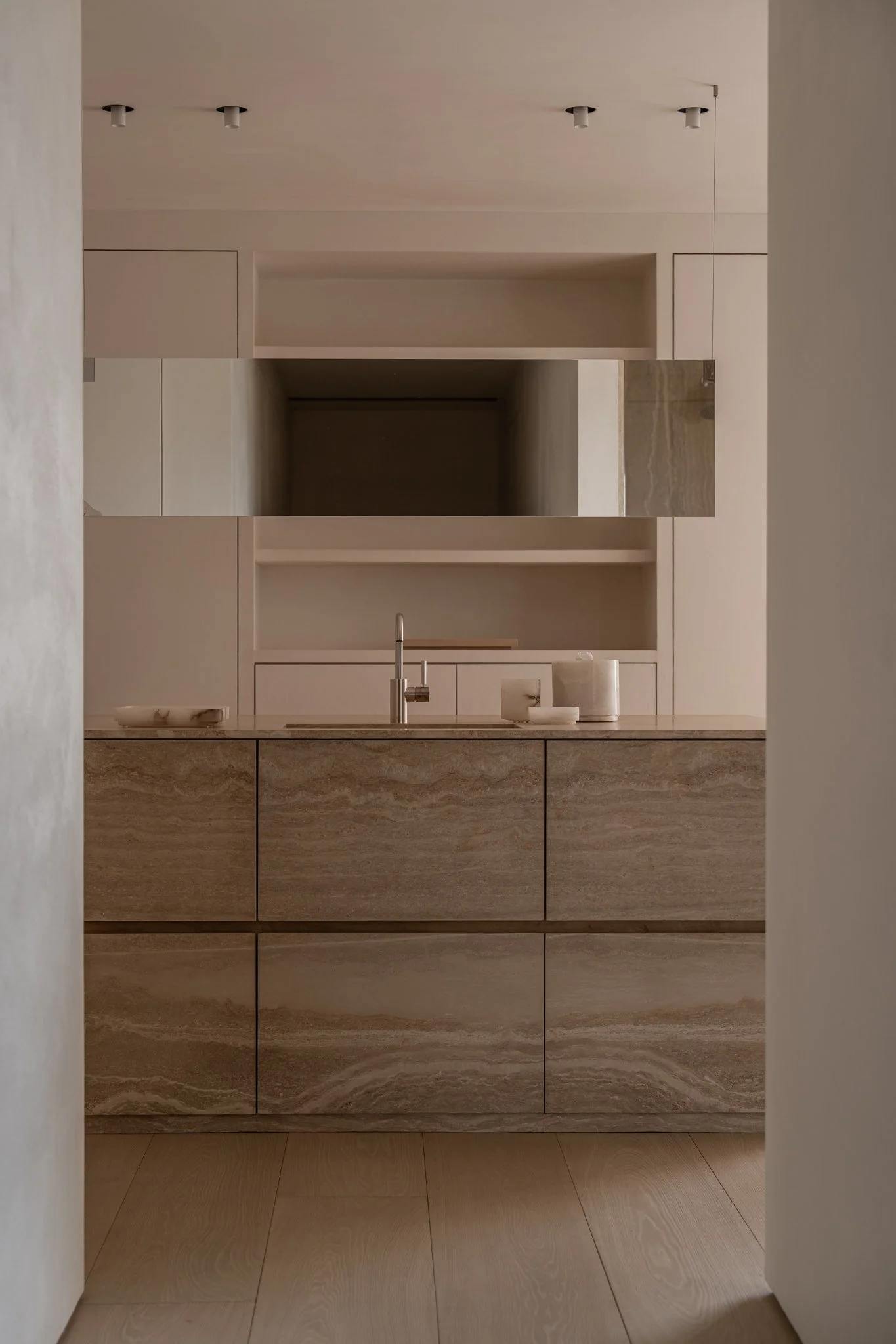 Minimalist kitchen with beige and brown marble cabinetry, a beige countertop, and a built-in mirror above the sink.