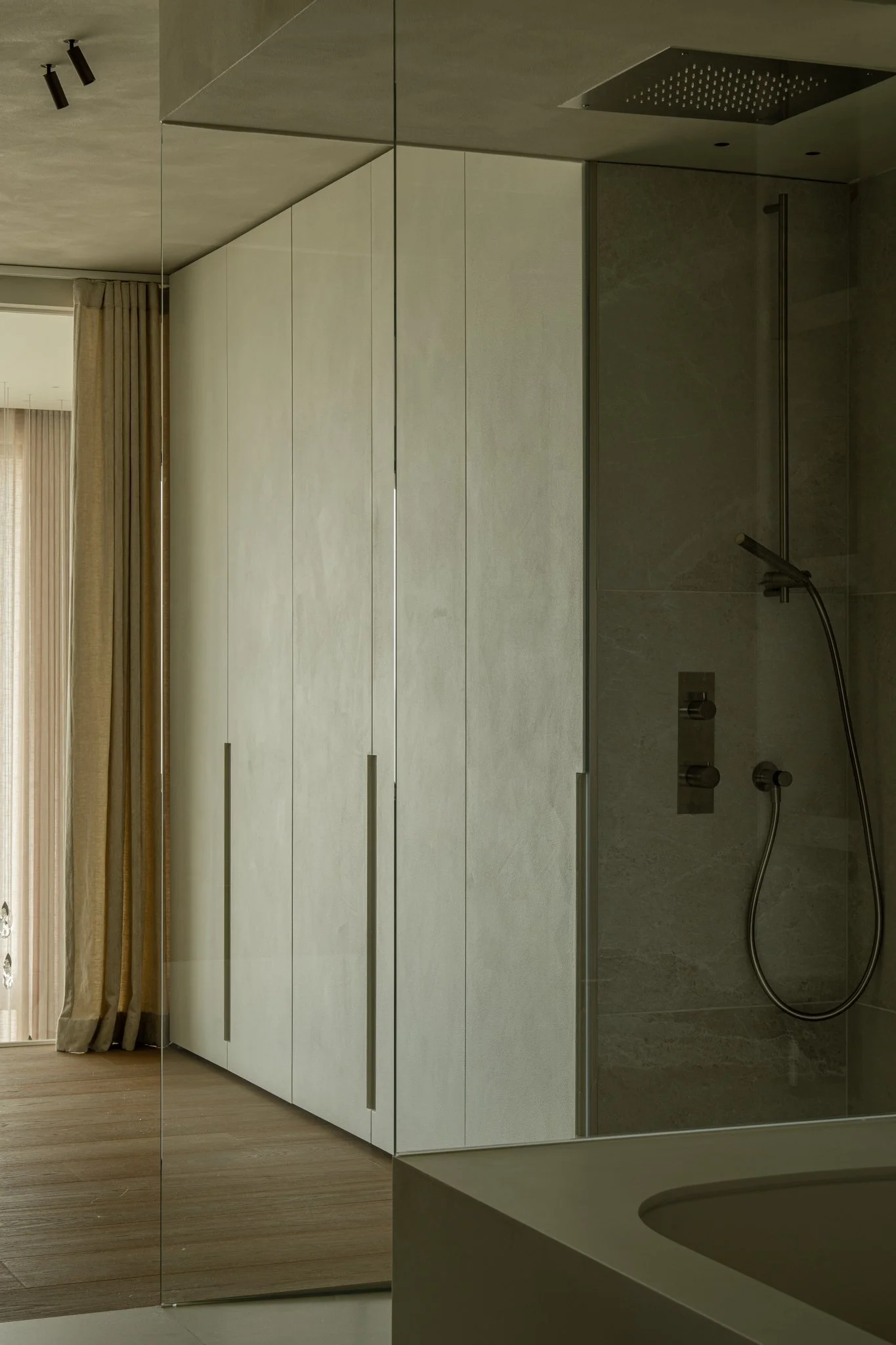 Modern bathroom with a shower, beige cabinets, and a mirror reflecting a window with curtains.