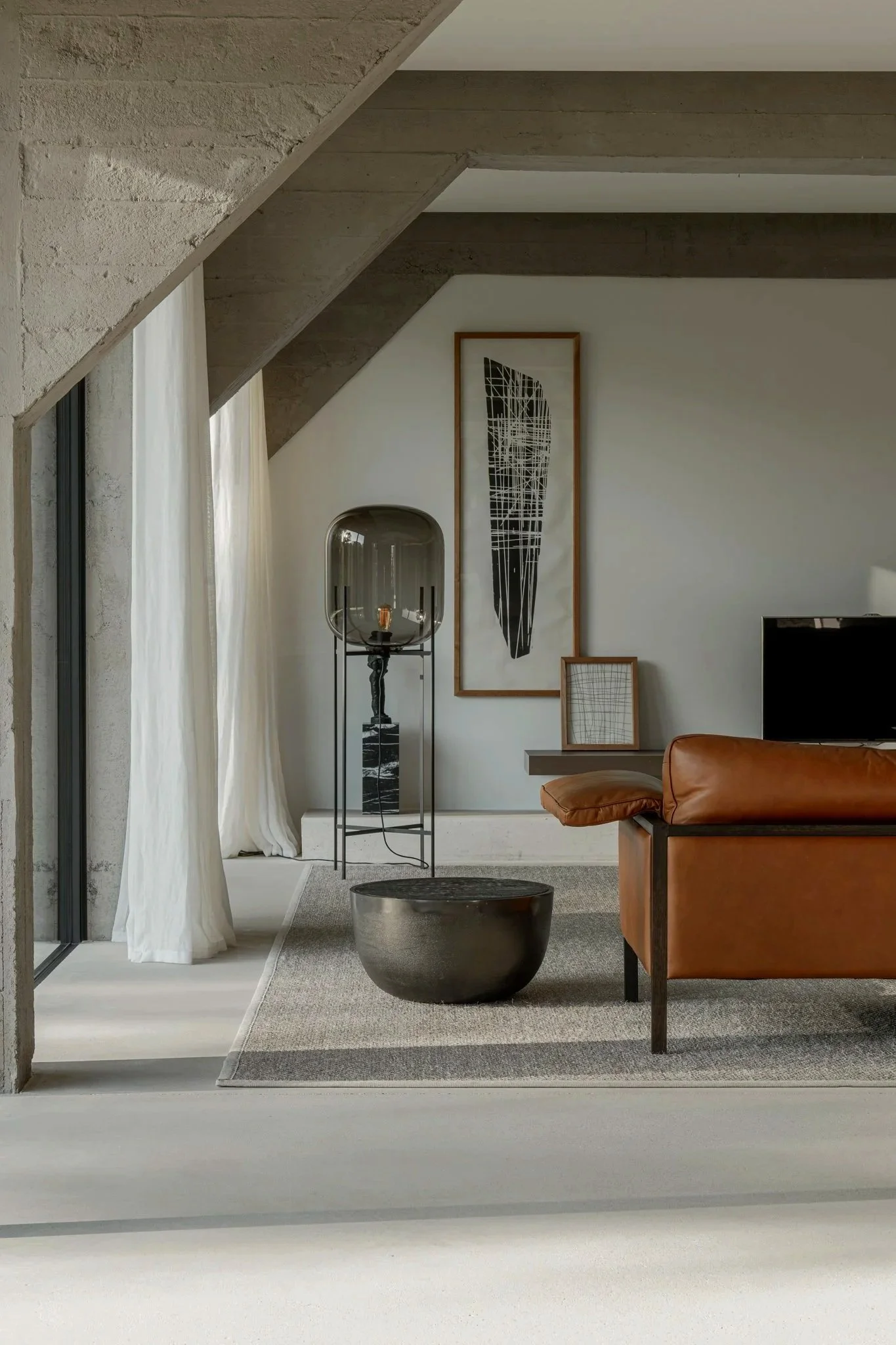 Modern living room with a leather sofa, abstract art, floor lamp, and large window with white curtains.