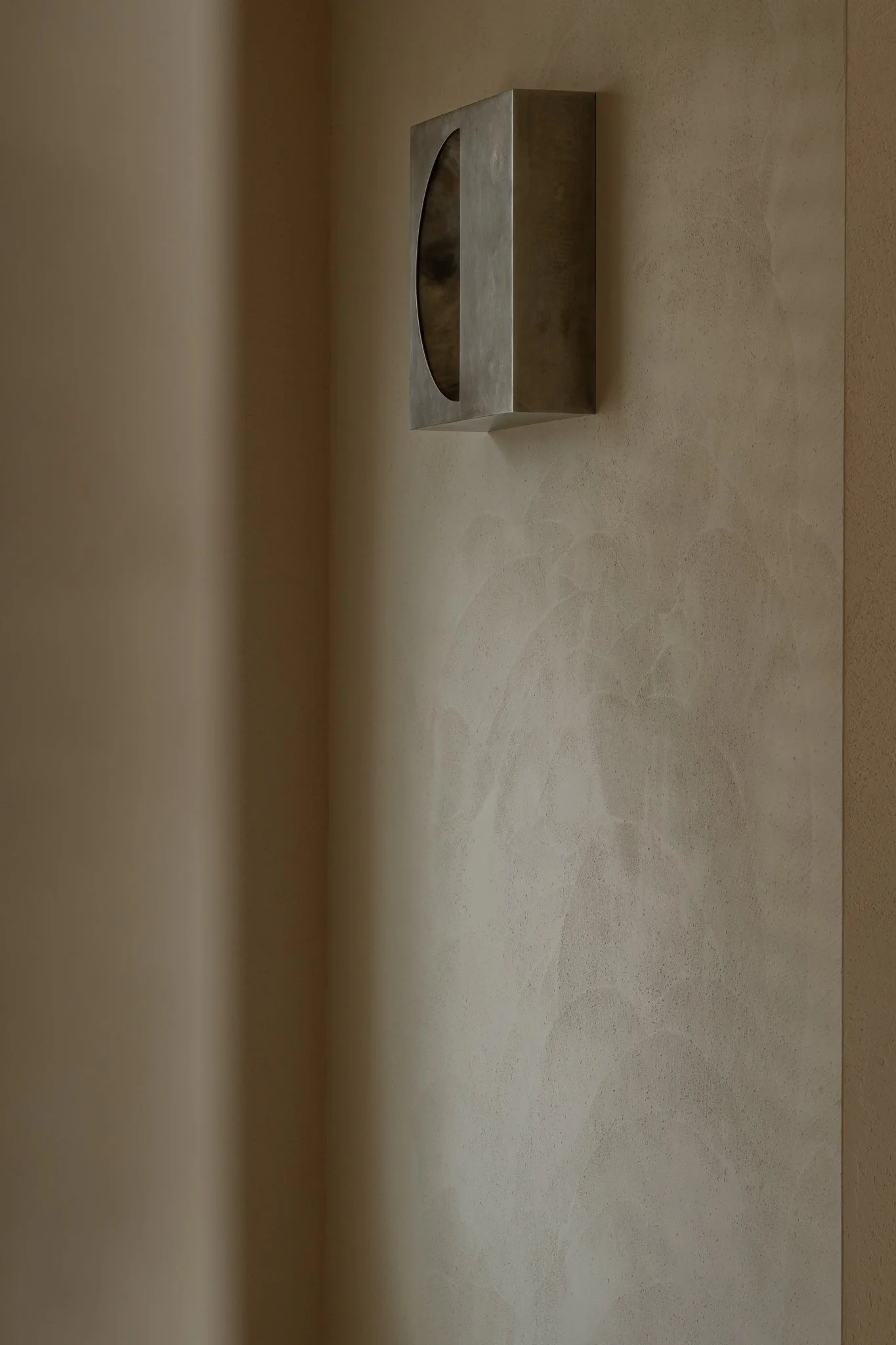 A minimalist wall-mounted fixture with a circular opening, hanging on a textured beige wall.
