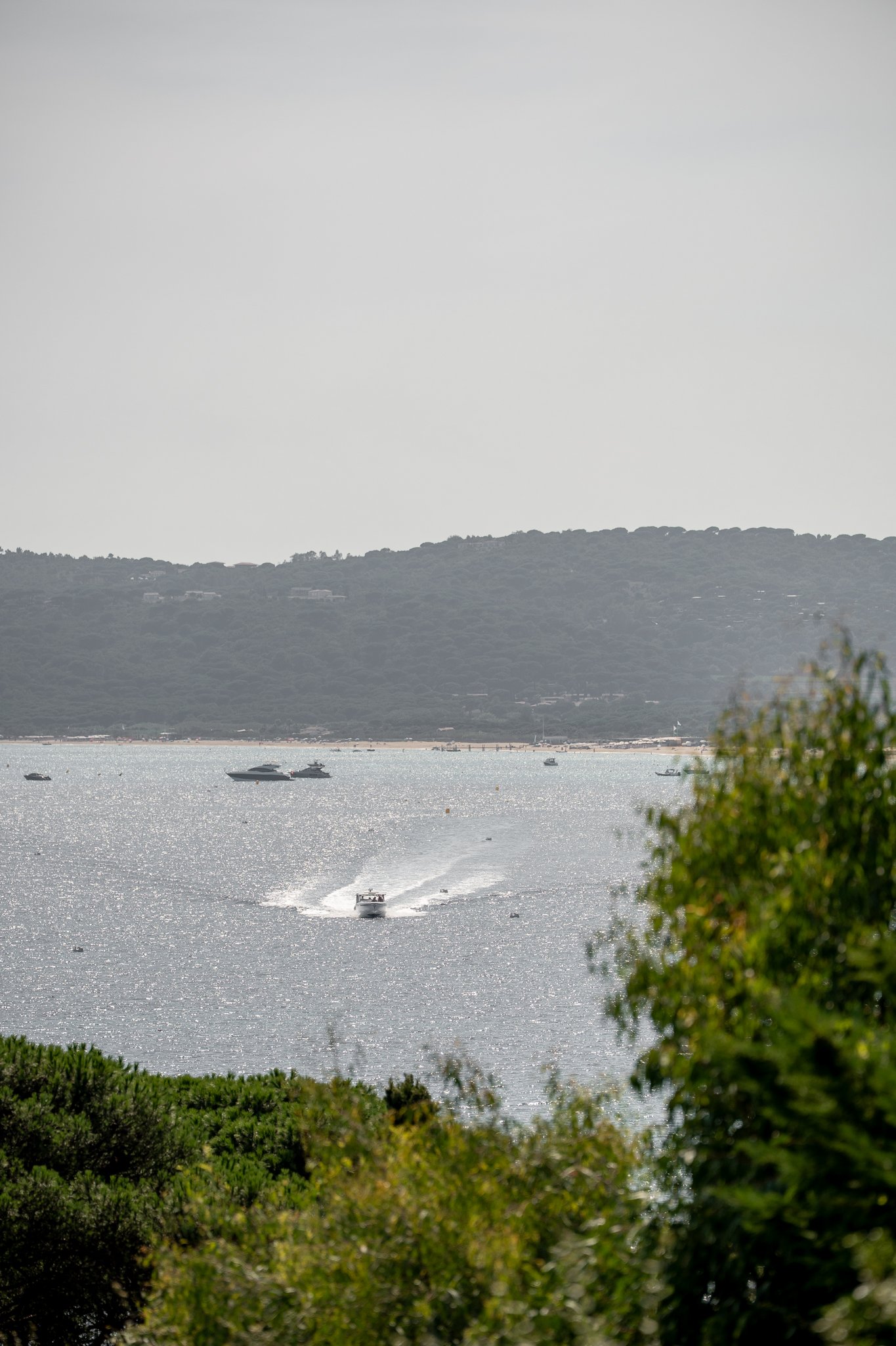 A body of water with boats, surrounded by trees and hills in the background.