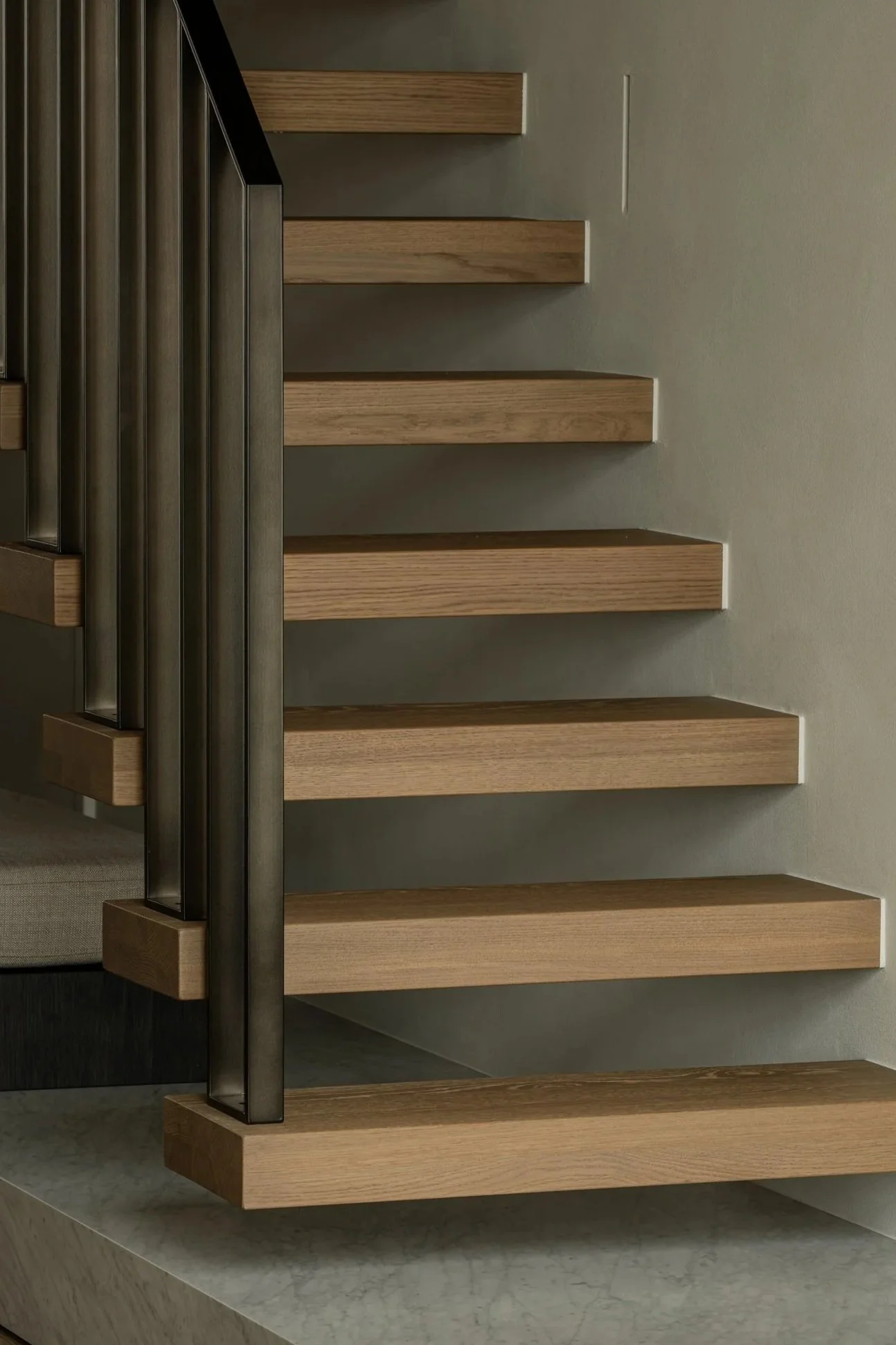 Close-up of a modern staircase with wooden steps and a black metal railing against a beige wall.