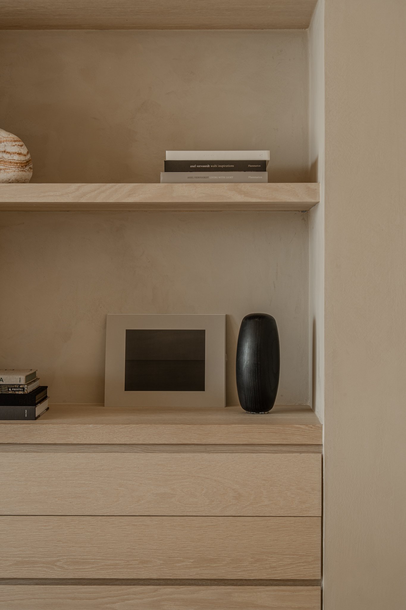 Minimalist wooden shelf with books, a black vase, and a picture frame.