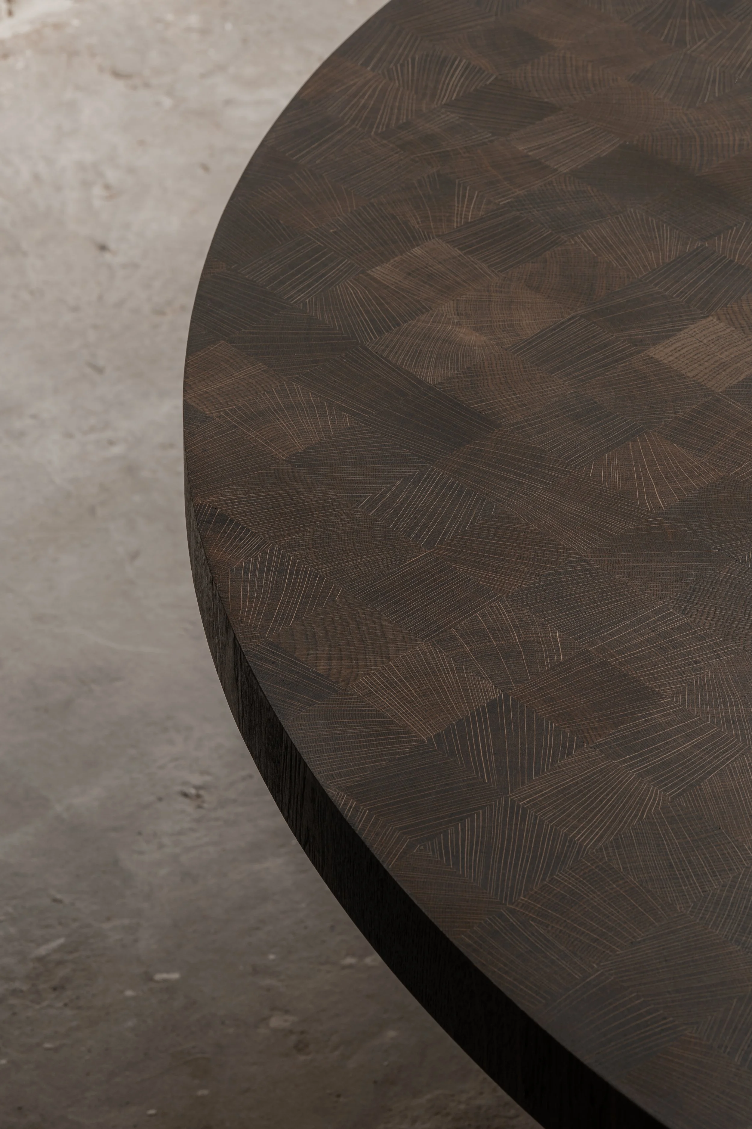 Close-up of a dark wooden table with intricate geometric pattern, set against a light, textured concrete floor.