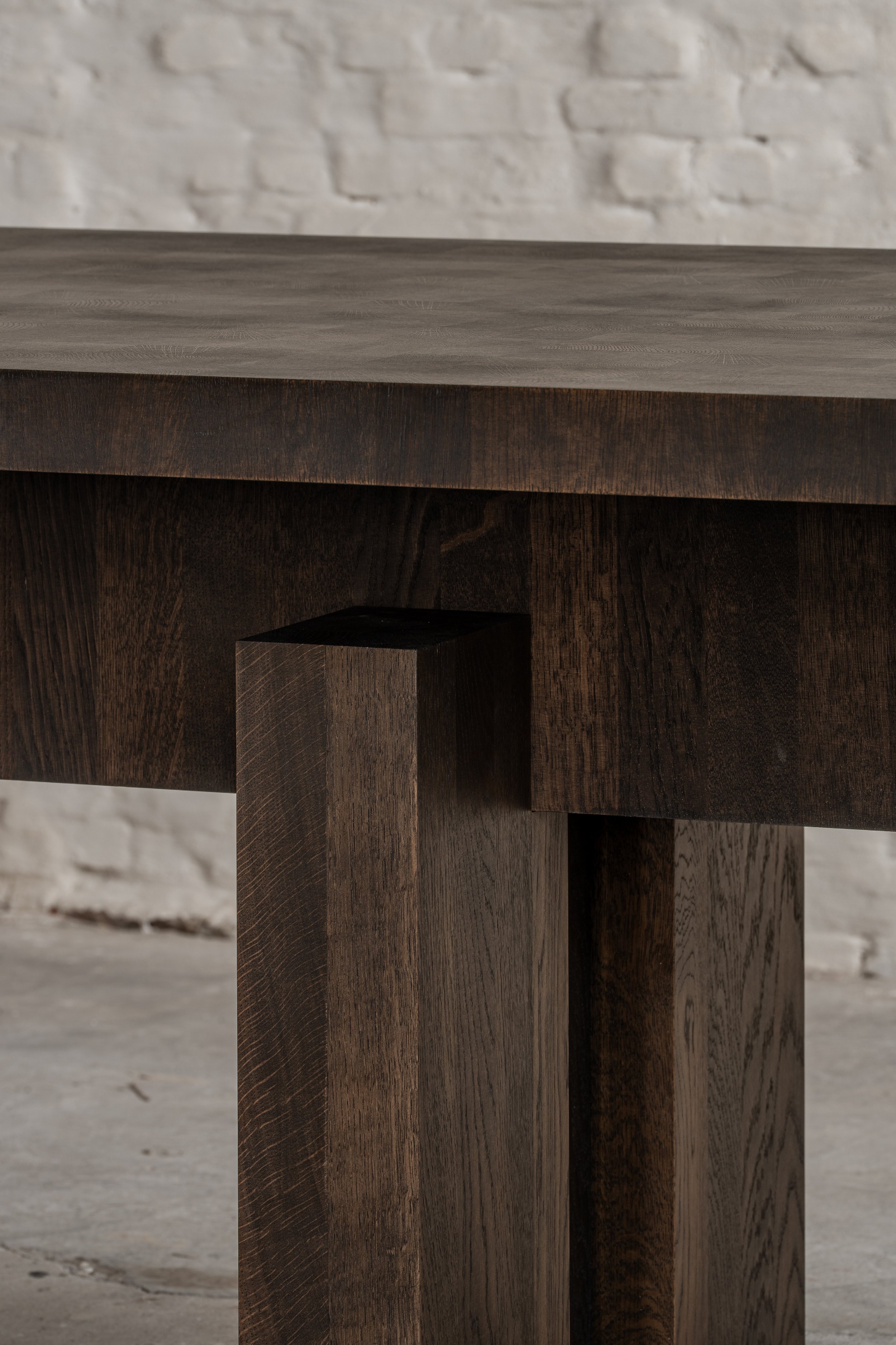 Close-up of a dark wooden table leg and edge with a white brick wall in the background.