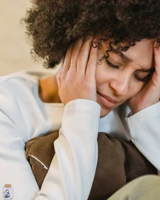 Woman with curly hair holding her head in hands, appearing stressed or tired.