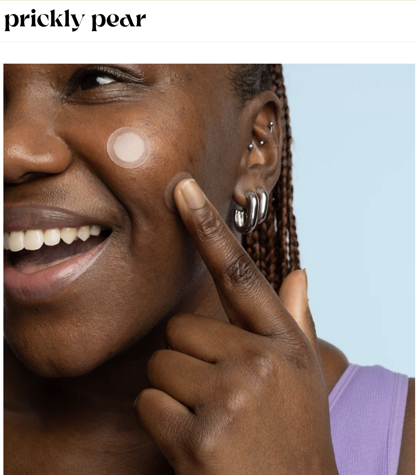 Tamara smiling with multiple ear piercings applies a round skincare patch to her cheek. for Prickly Pear Skin Care