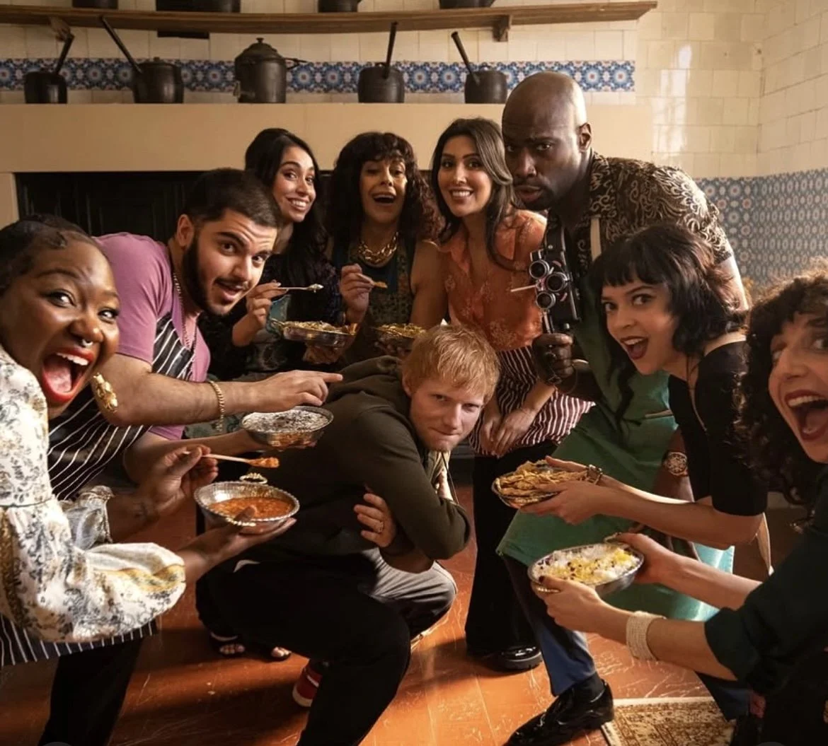 A diverse group of people gathered around a table at a festive dinner, smiling and enjoying food together in a warmly decorated room.