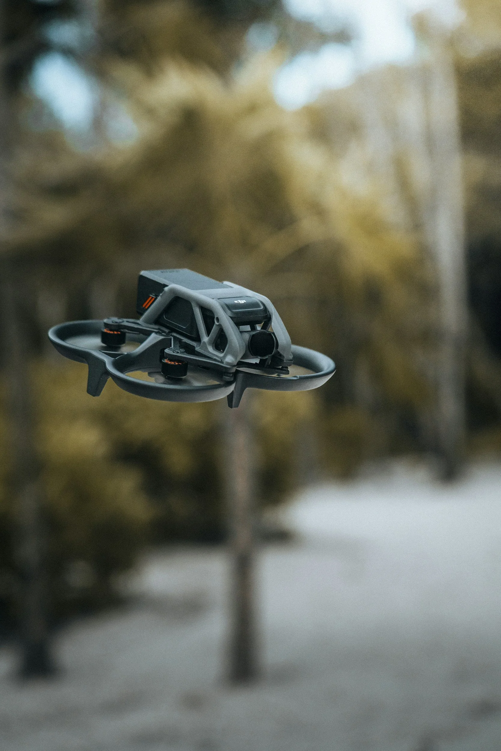 A compact drone flying outdoors with a blurred forest background.
