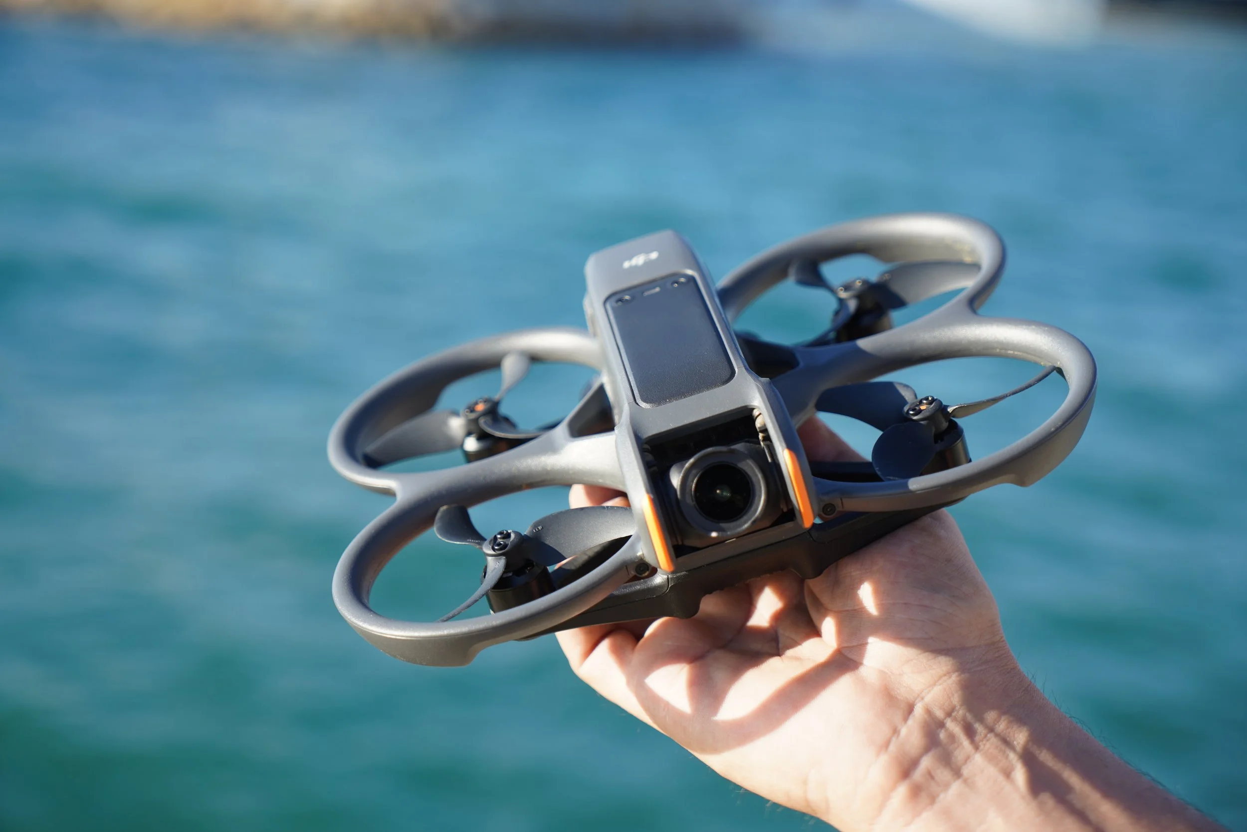 A small drone flying outdoors with a blurred forest background.