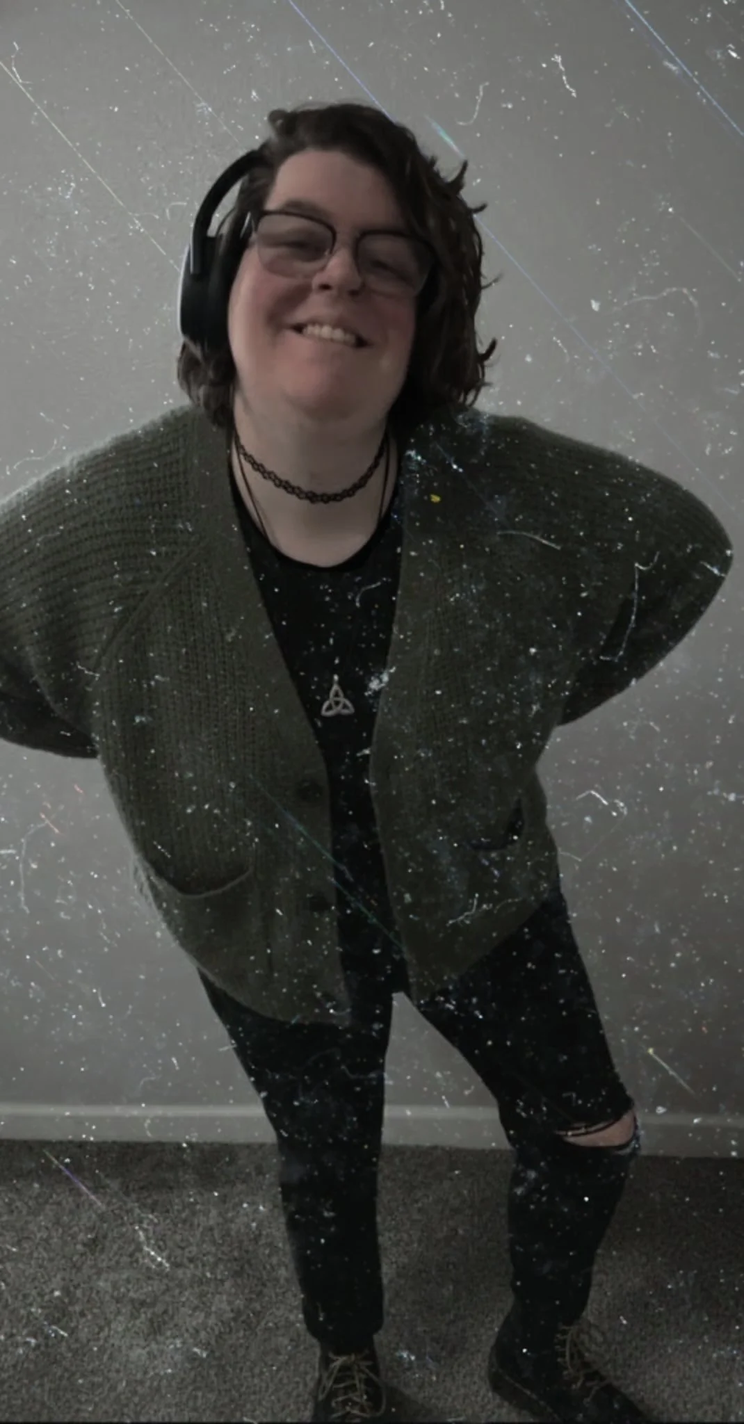 Rachel, founder of Oktober Designs, smiling and wearing headphones and a choker necklace against a textured light background