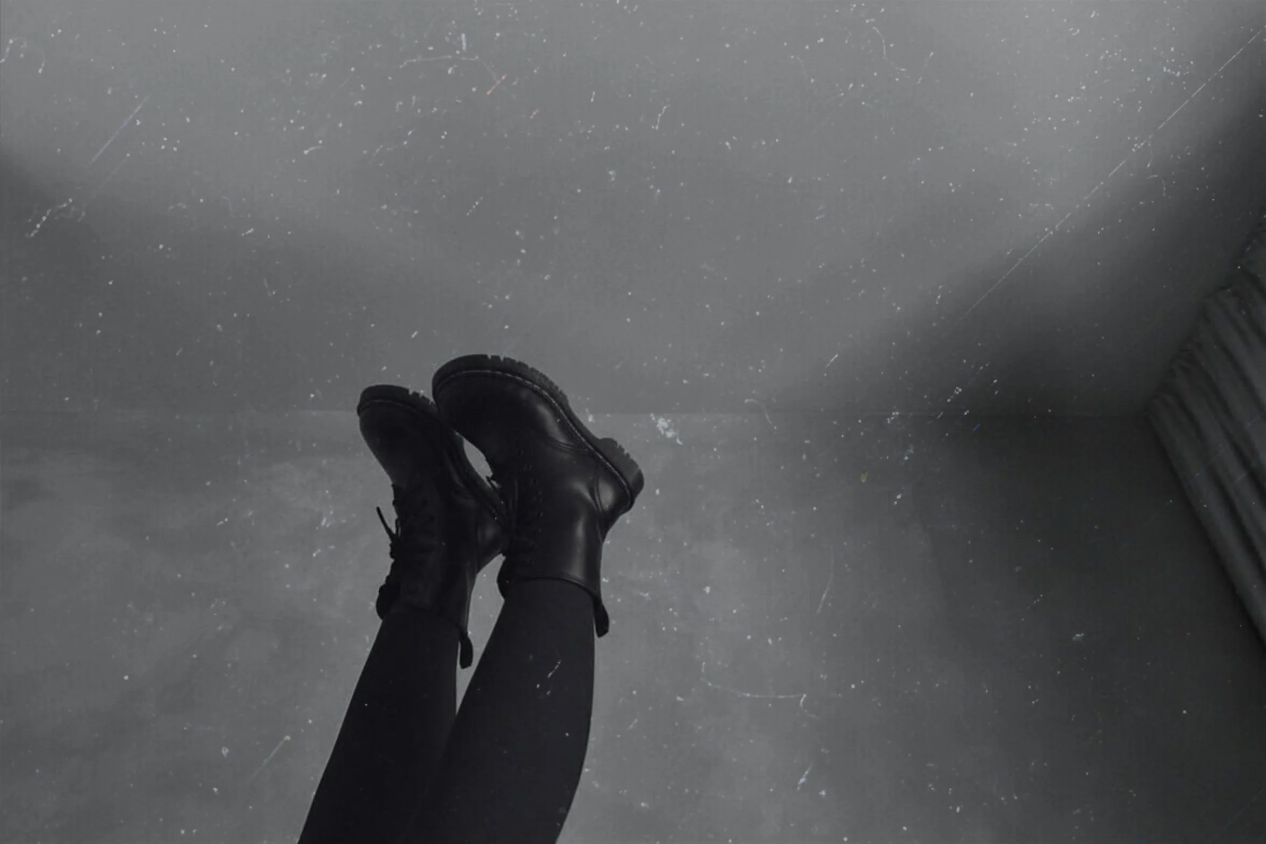Black lace-up boots raised against a grey textured sky with light film grain overlay