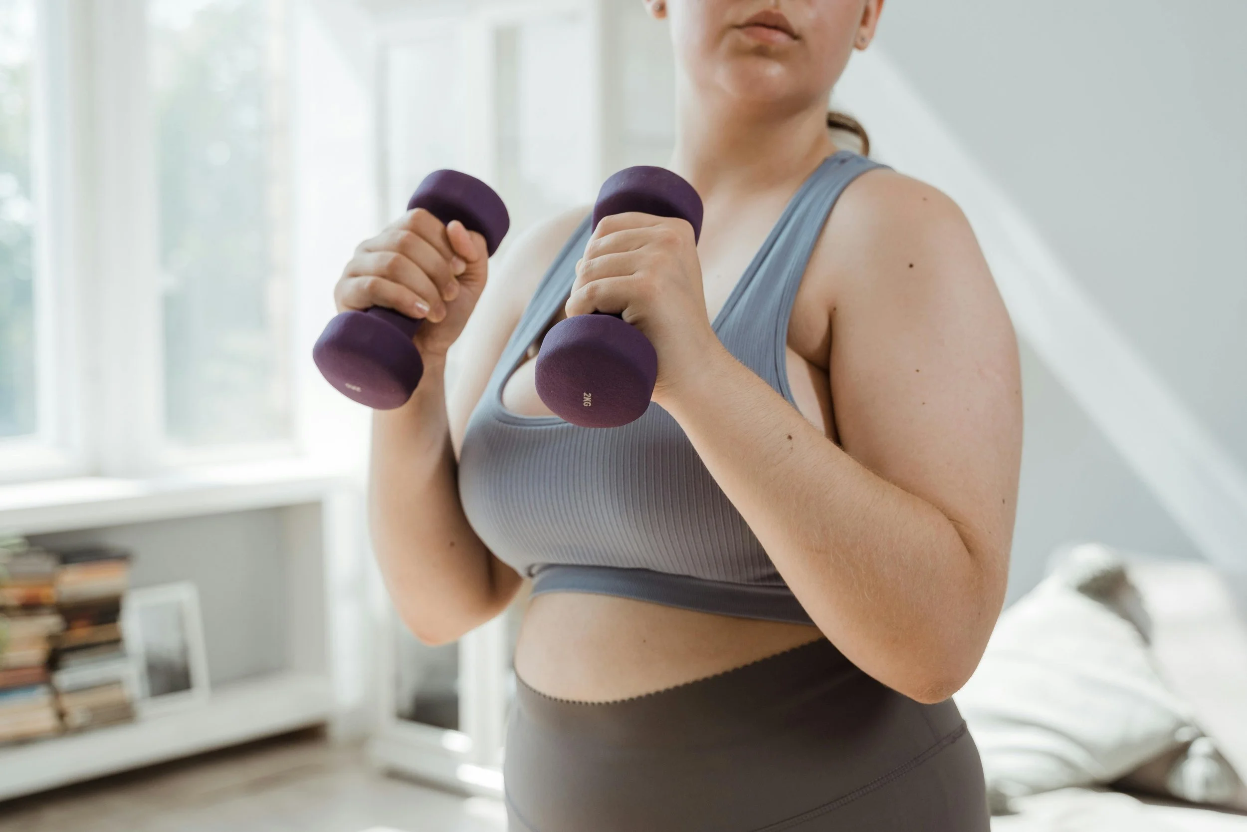 Woman lifting weights during a personal training session focused on nervous system support, recovery from burnout, movement trauma, and chronic stress, emphasizing rest, rhythm, and rebuilding trust in the body.