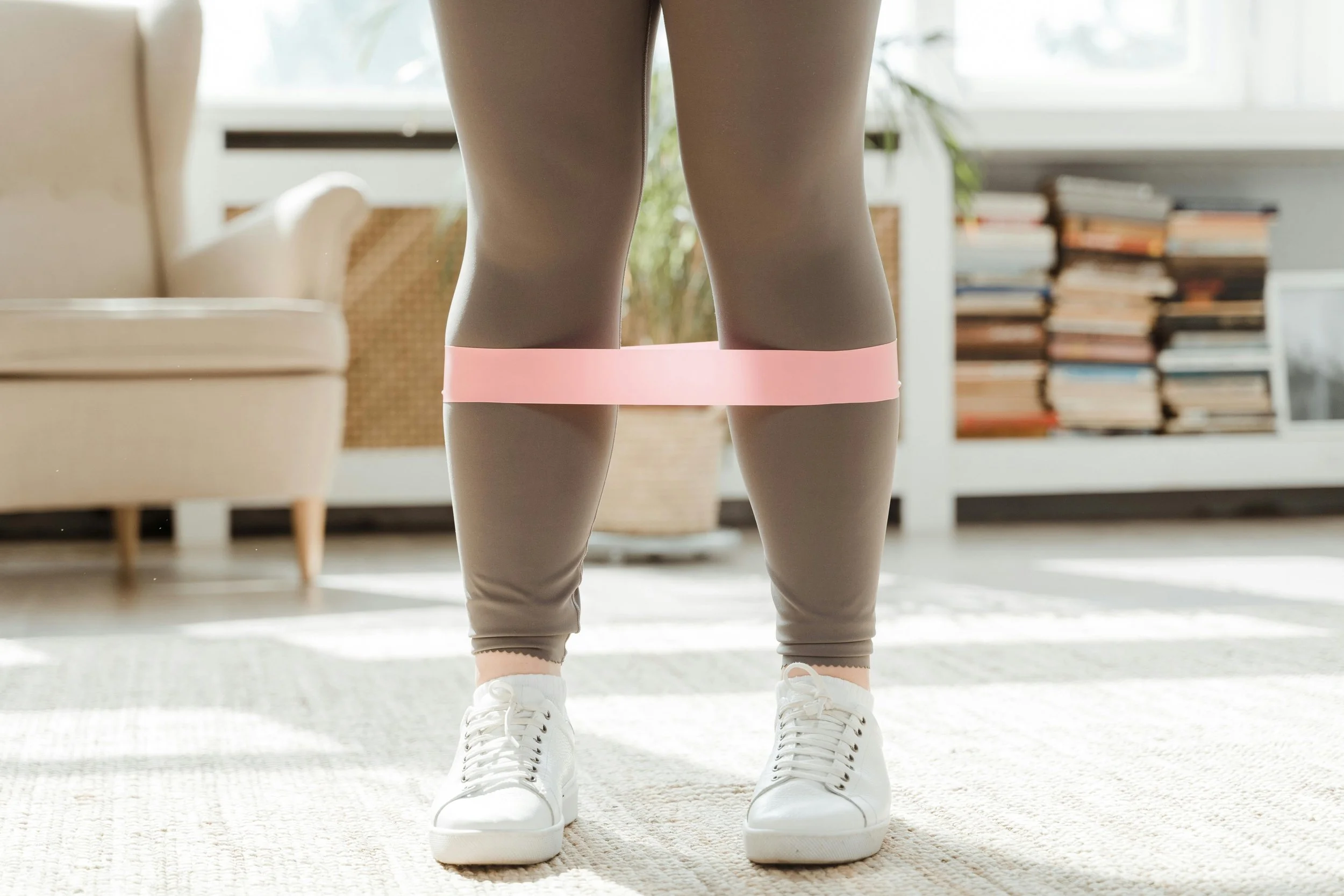 A woman stands with resistance bands around her legs—symbolizing strength, grounding, and the empowering process of reconnecting with the body through intentional movement.