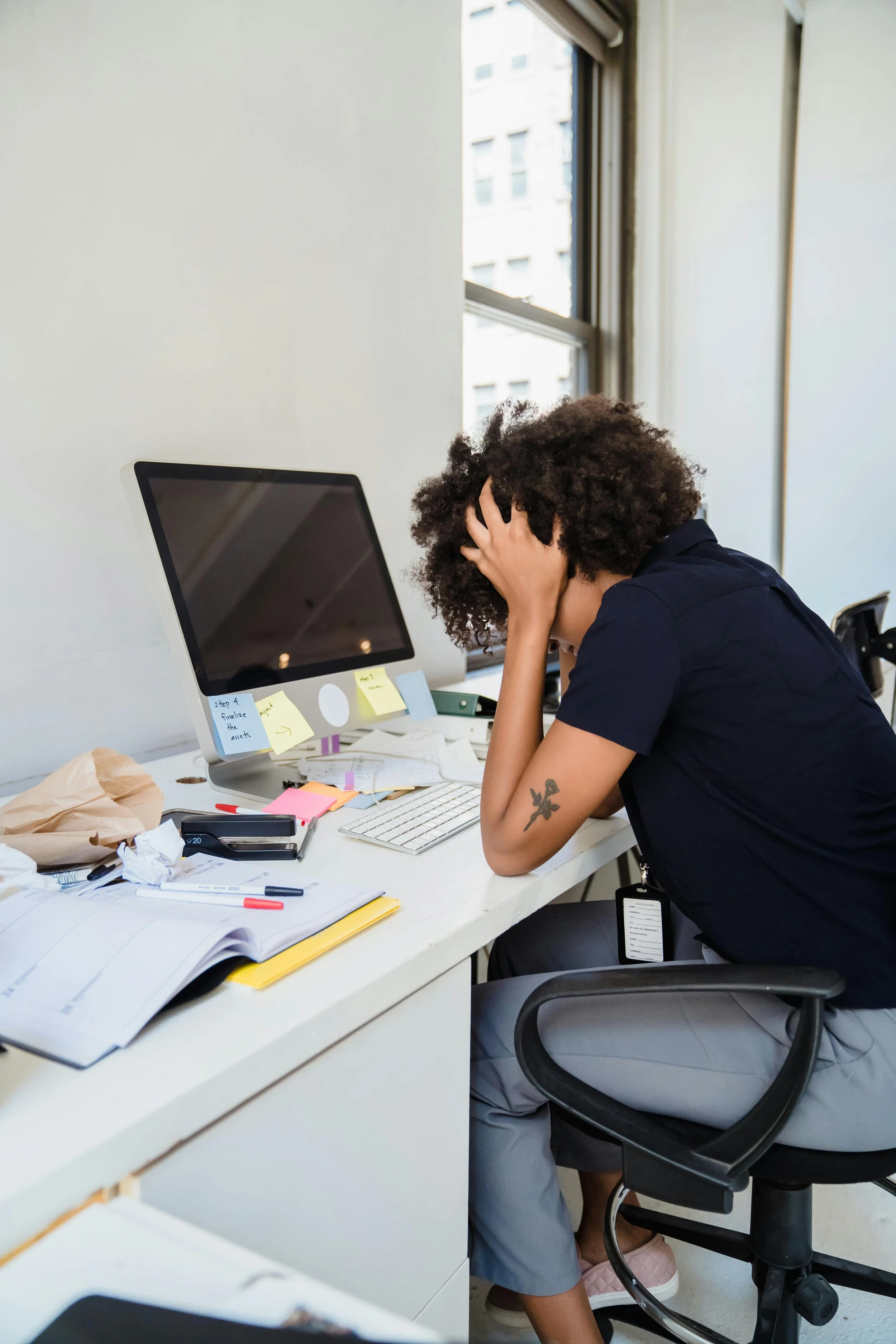 A person sits at a desk in front of a computer, head resting in their hands—conveying feelings of overwhelm, tension, and emotional fatigue often tied to anxiety and stress.