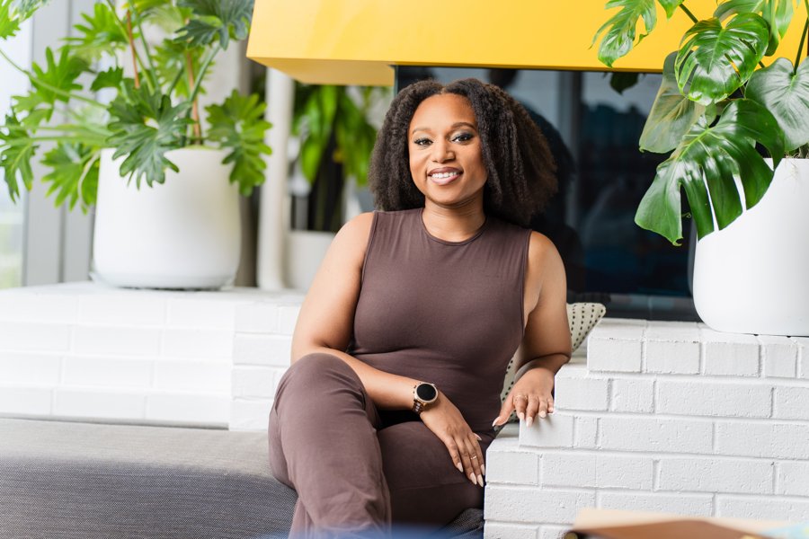 Meagé Clemments, the Unbothered Therapist®, sitting and smiling warmly, welcoming clients seeking collaborative wellness and compassionate therapy.