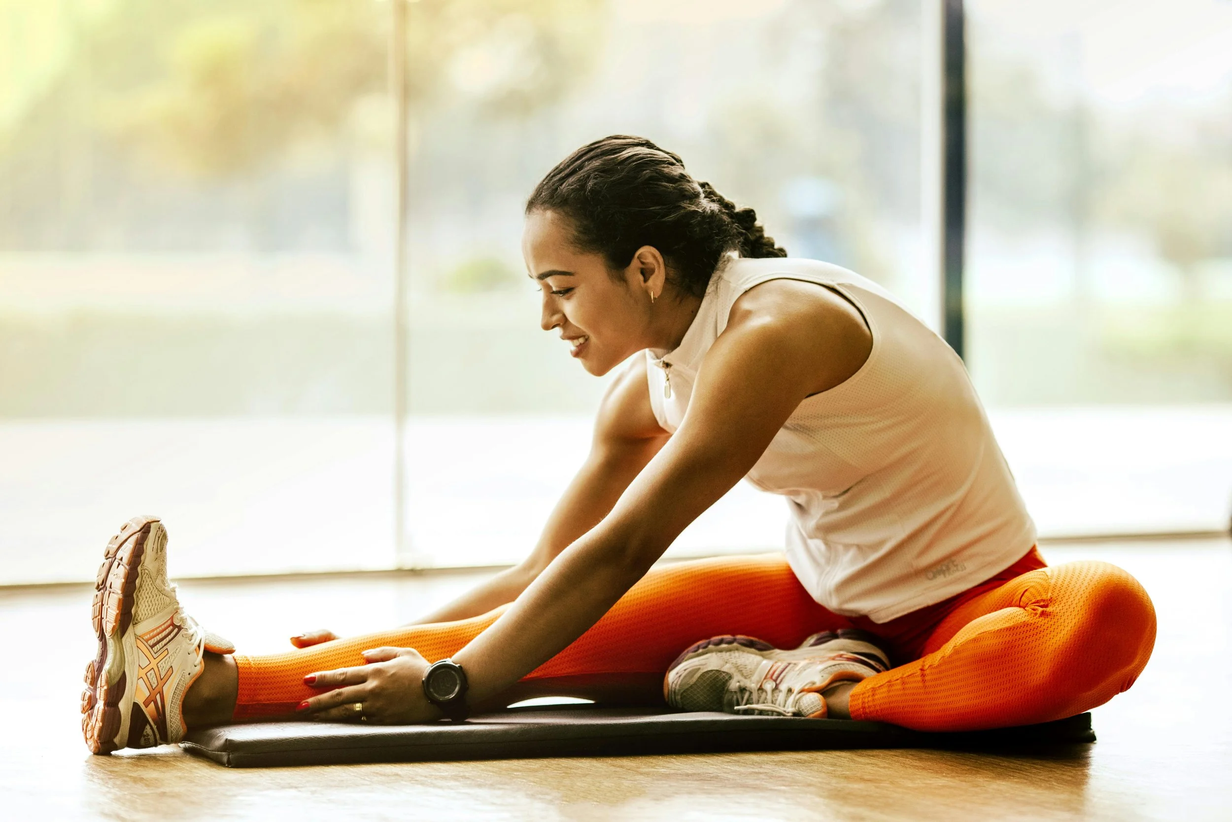 A woman sits on the floor, smiling as she stretches her legs—reflecting joyful, accessible movement and the process of rebuilding trust with the body through trauma-informed care.