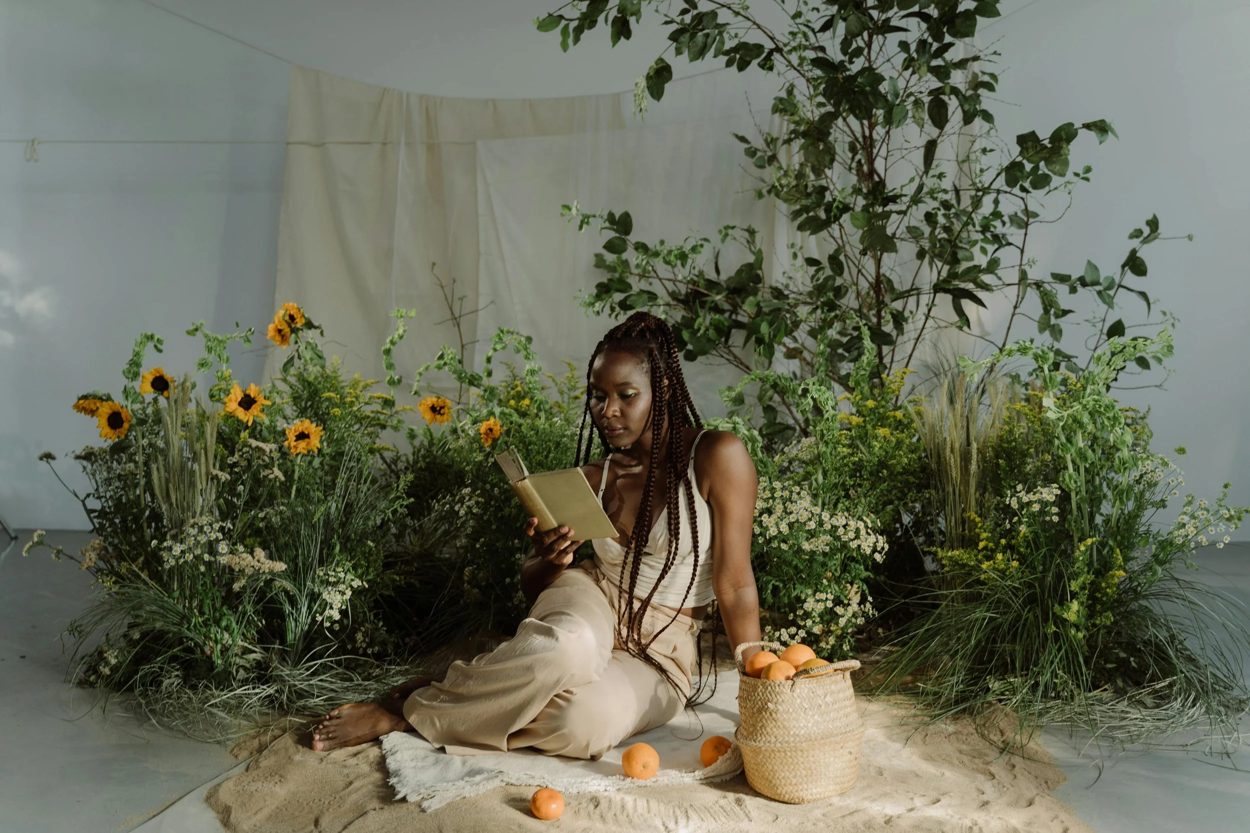 Woman of color reading in a peaceful, flower-filled space, reflecting trauma-informed healing and nervous system regulation