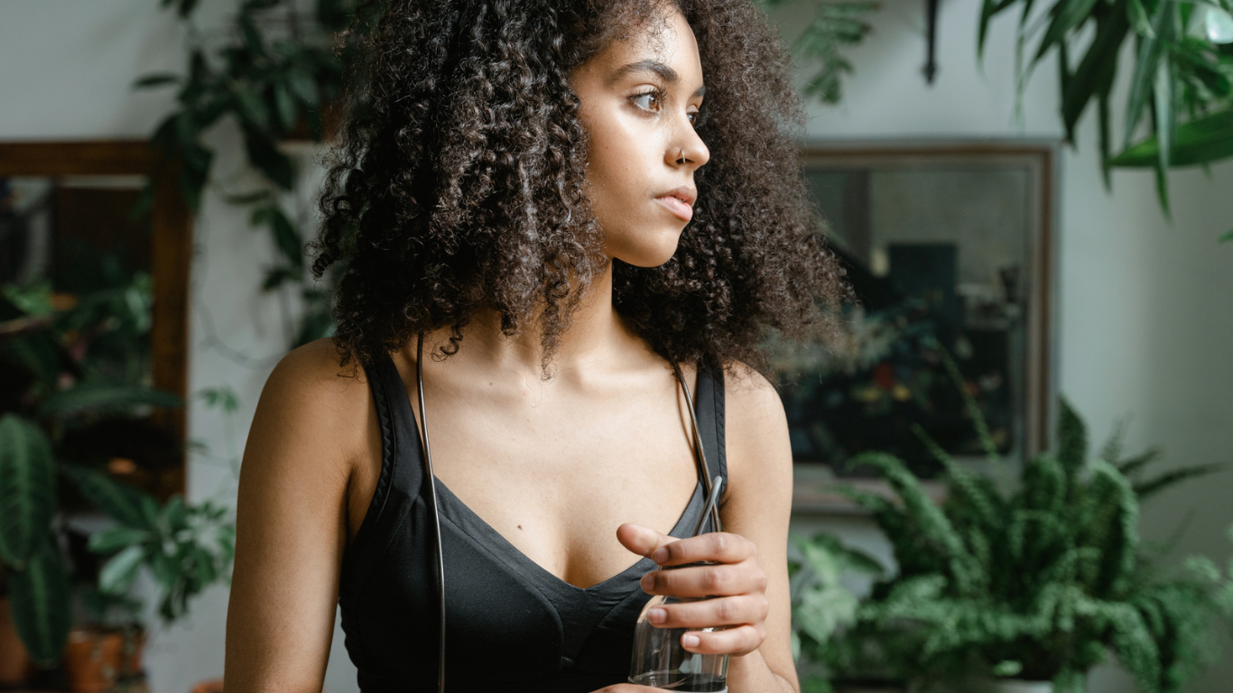 A woman of color stands in quiet reflection, sunlight streaming in through the window.