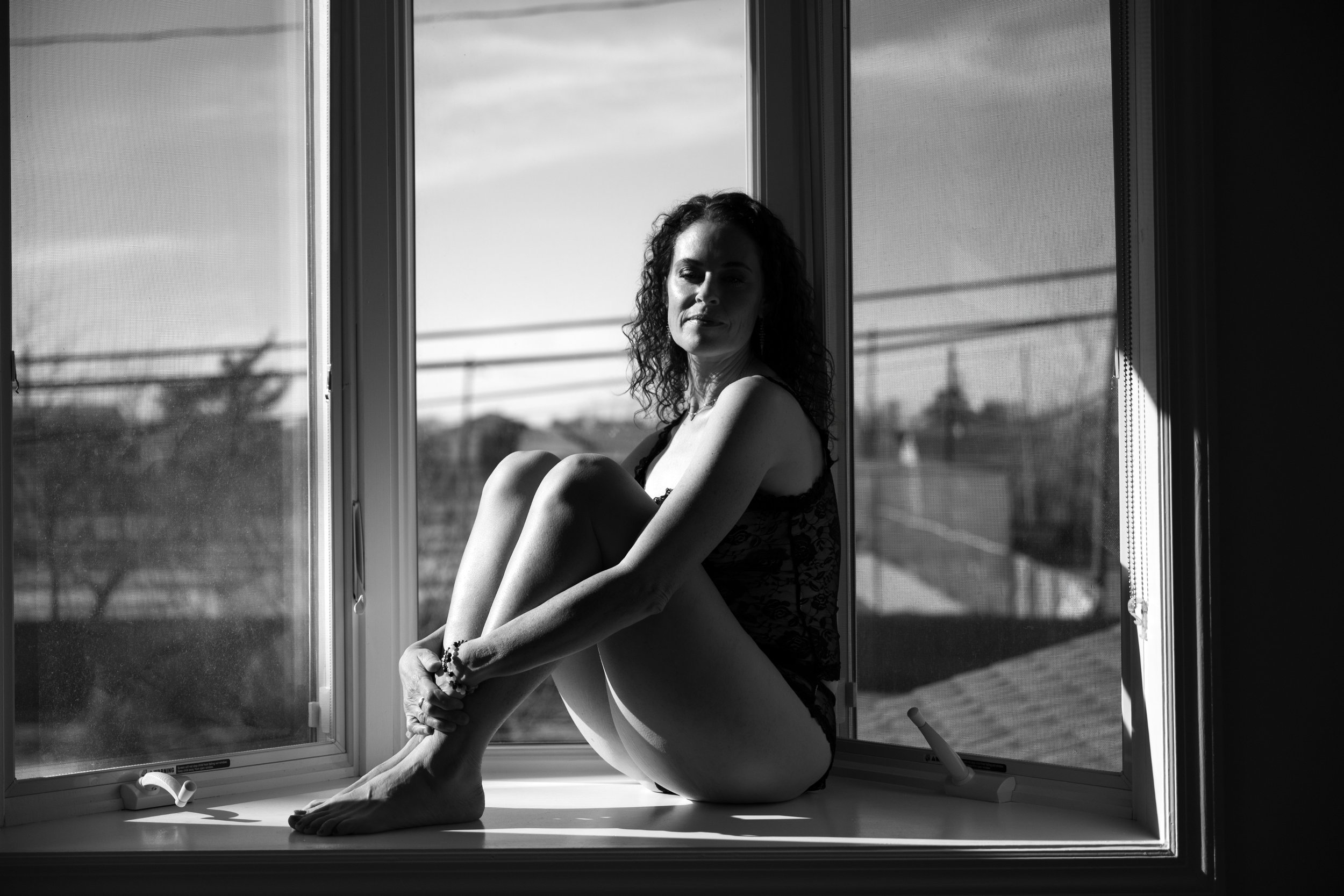 Quiet portrait of a woman seated on a window sill by Eye Candy Boudoir, capturing a woman owning her moment.