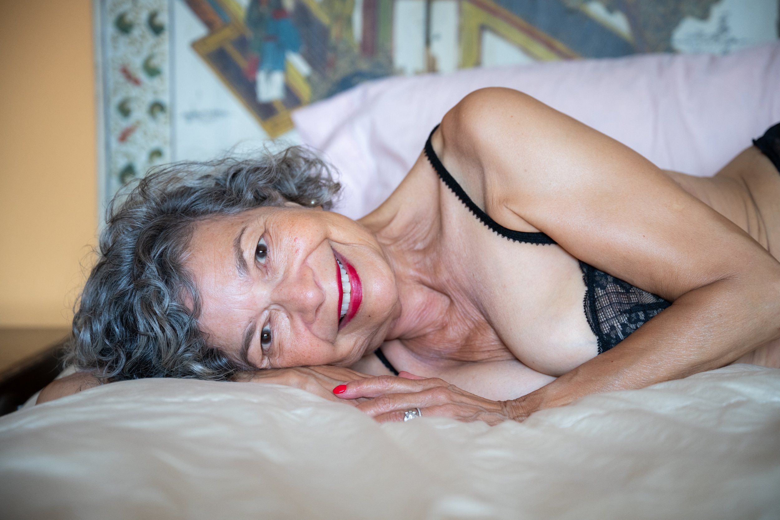 Relaxed image of a mature, smiling woman lying on her side in a bedroom in New York City. 