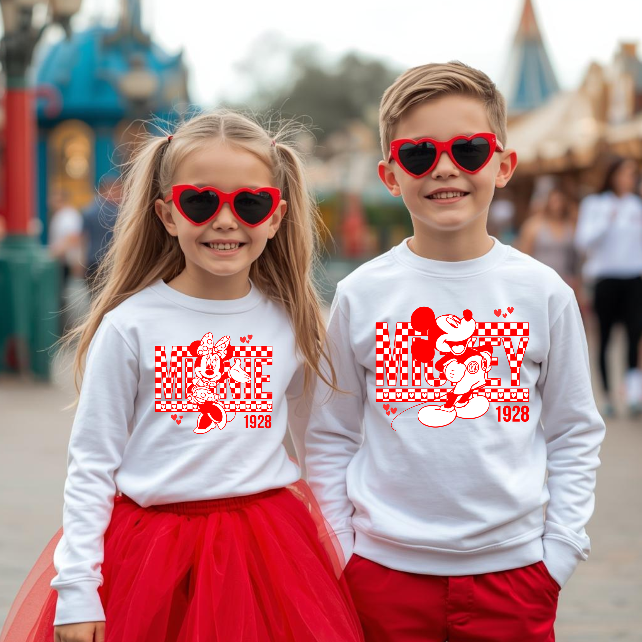 Two children, a girl and a boy, wearing white sweatshirts with Minnie Mouse and Mickey Mouse designs, red sunglasses, and red clothing, standing in an amusement park or carnival setting.