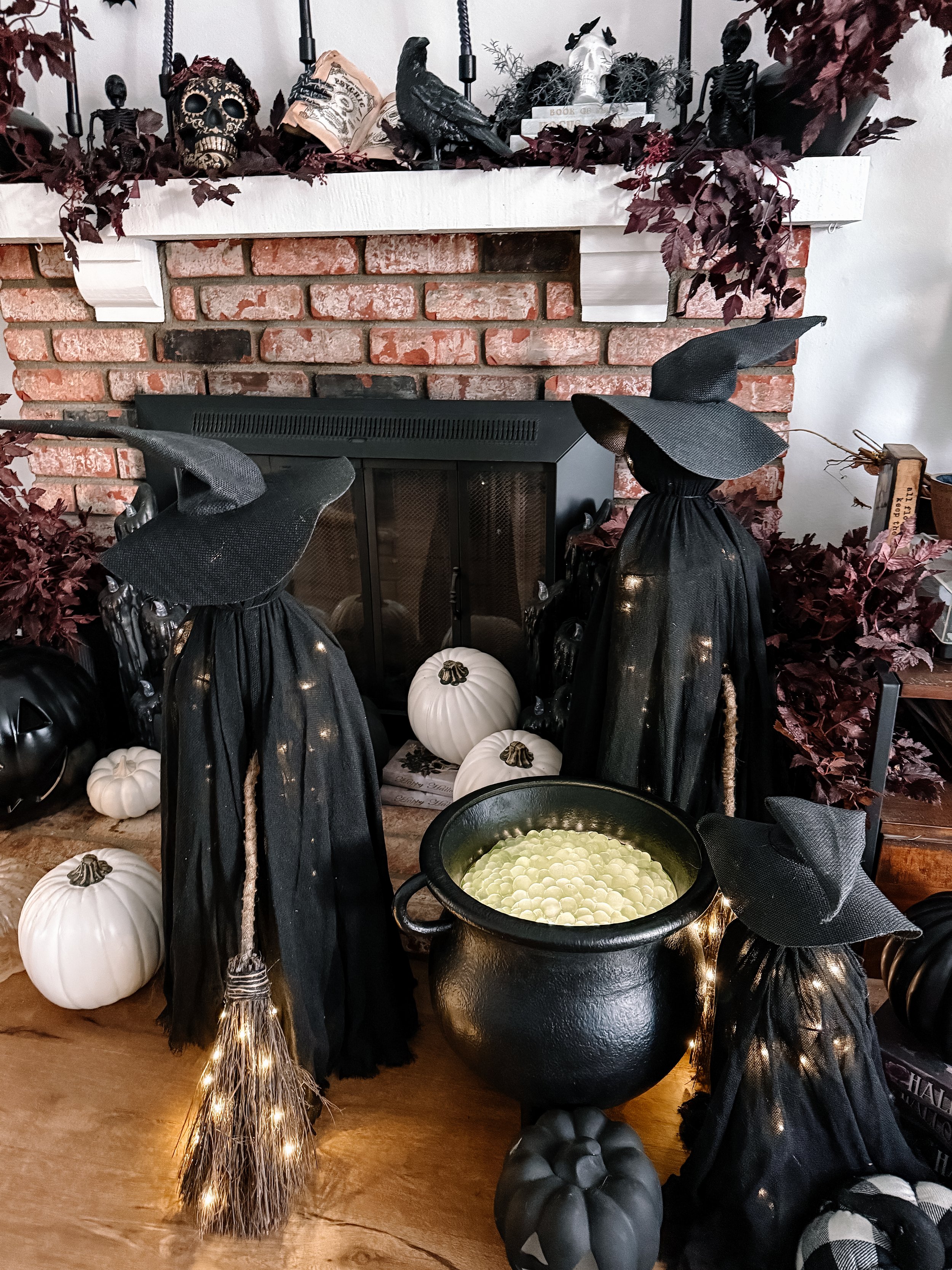 Decorated fireplace with Halloween decorations including black witches' hats, faux pumpkins, black crows, skulls, and autumn leaves.