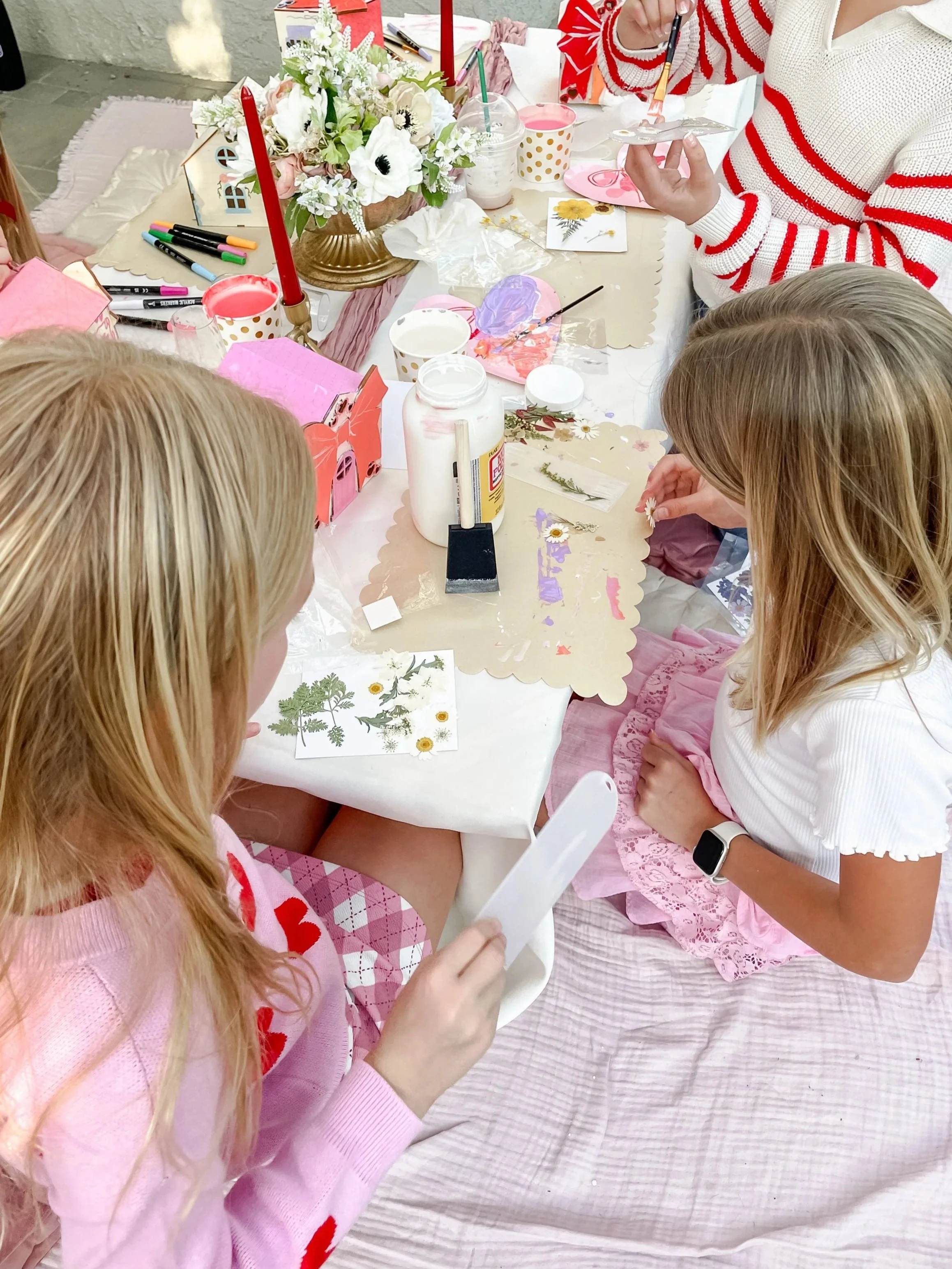 Children engaging in a craft activity at a table decorated with flowers, candles, and craft supplies, including glue and paper cuttings.