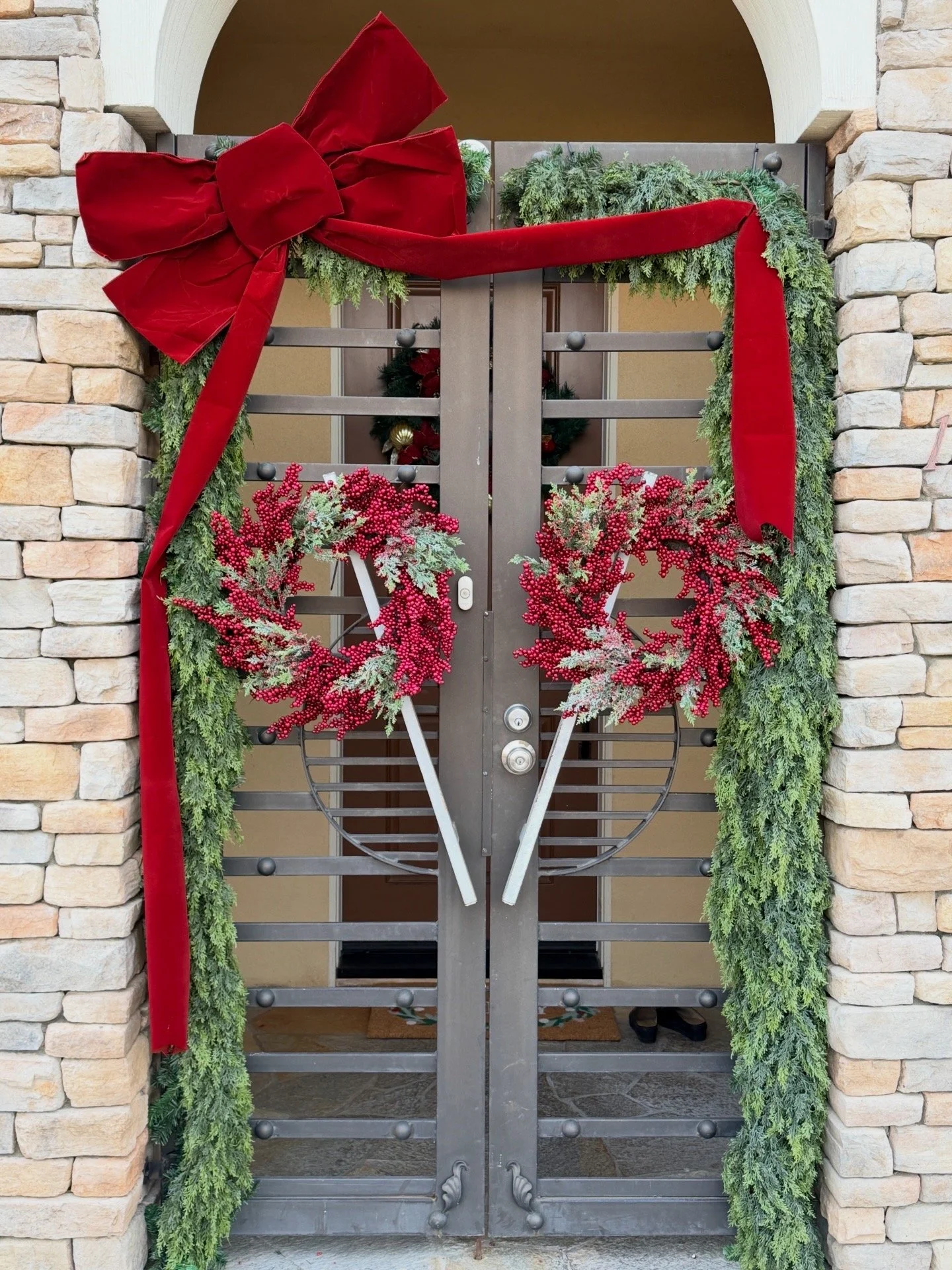 Decorated front door with a red bow, green garland, red berries, and wreaths for Christmas.