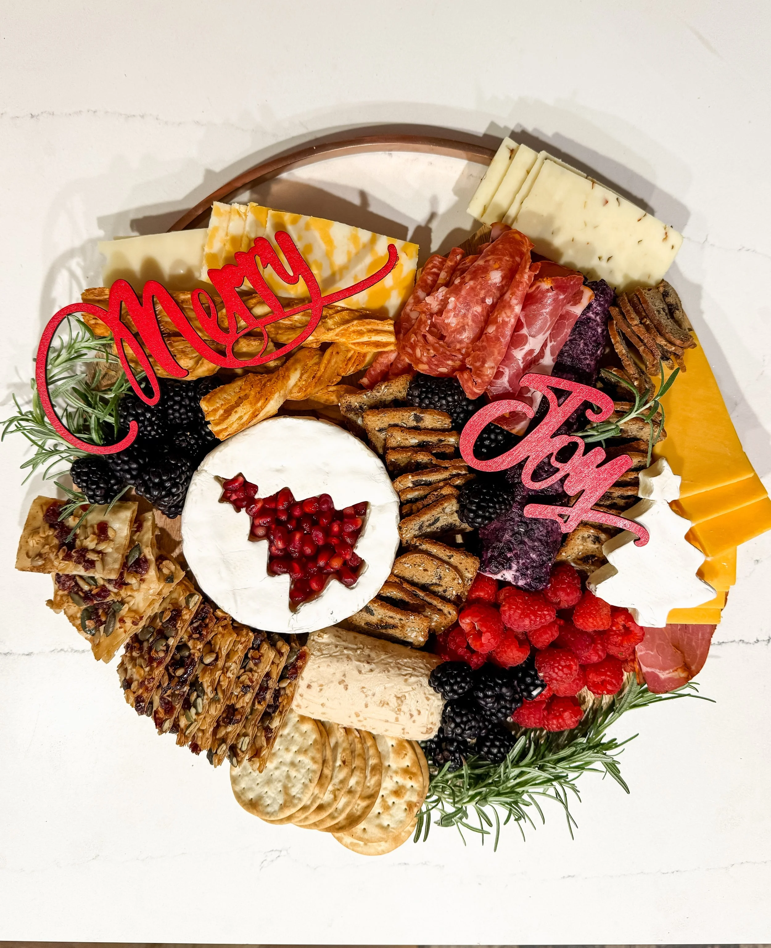 A Christmas cheese and charcuterie board with various cheeses, meats, crackers, and berries, decorated with "Merry