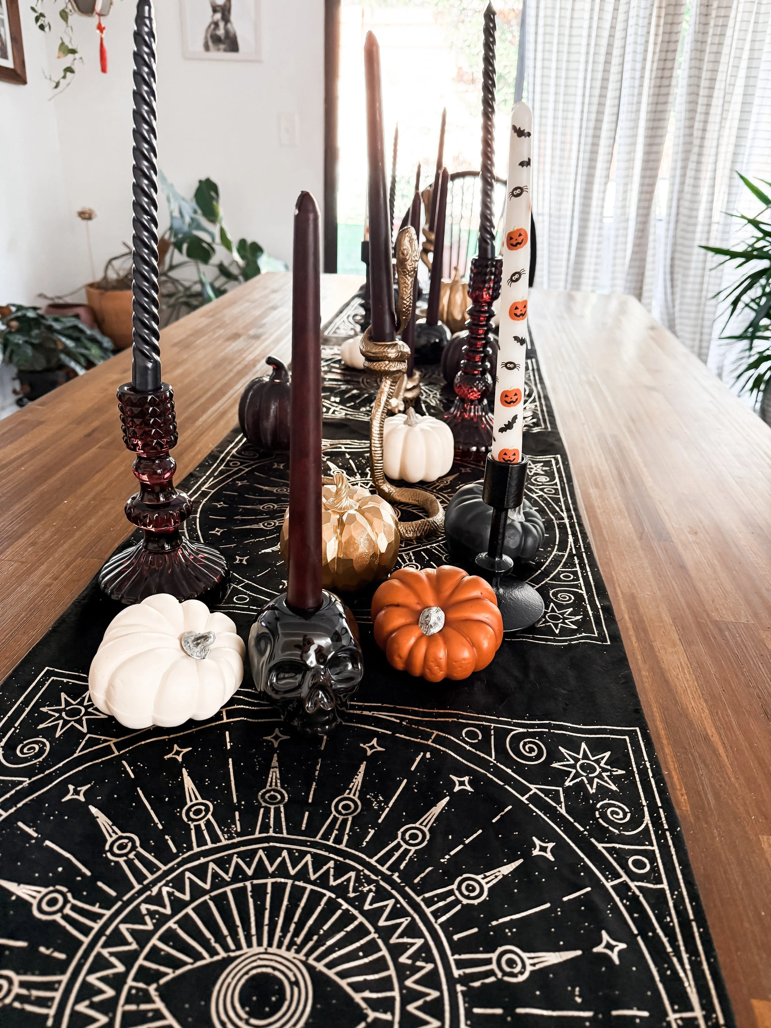 Table runner with Halloween-themed candles and small pumpkins on a wooden table.