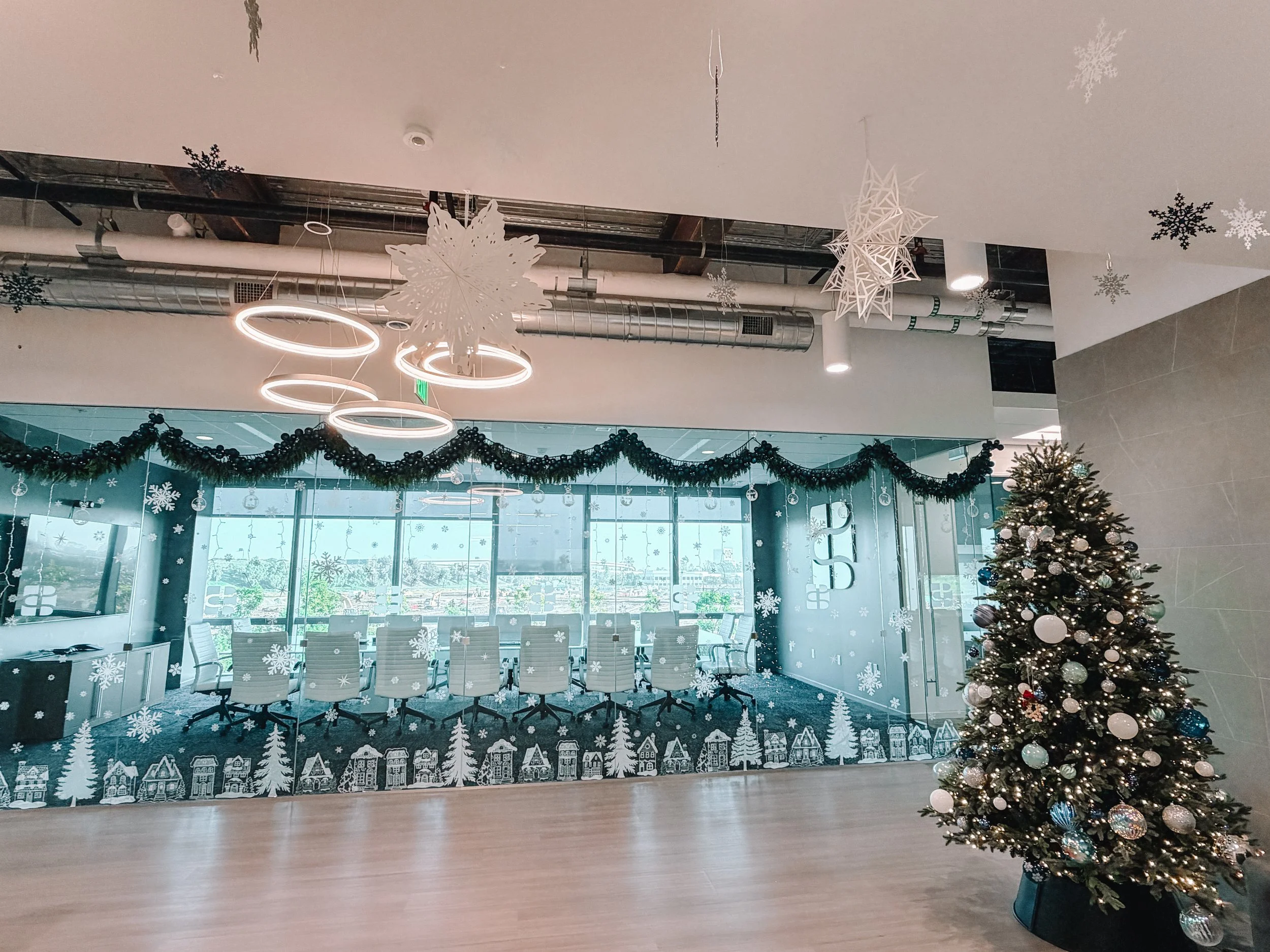 Office conference room decorated for Christmas with a Christmas tree, winter-themed window decals, and holiday garlands.