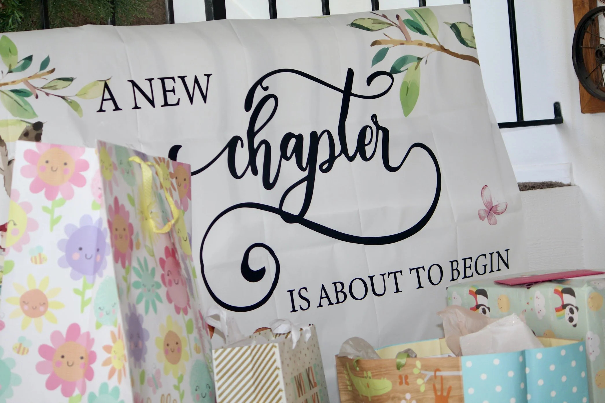 Decorations for a baby shower with a large white banner that says 'A new chapter is about to begin', surrounded by colorful gift bags with cheerful patterns.