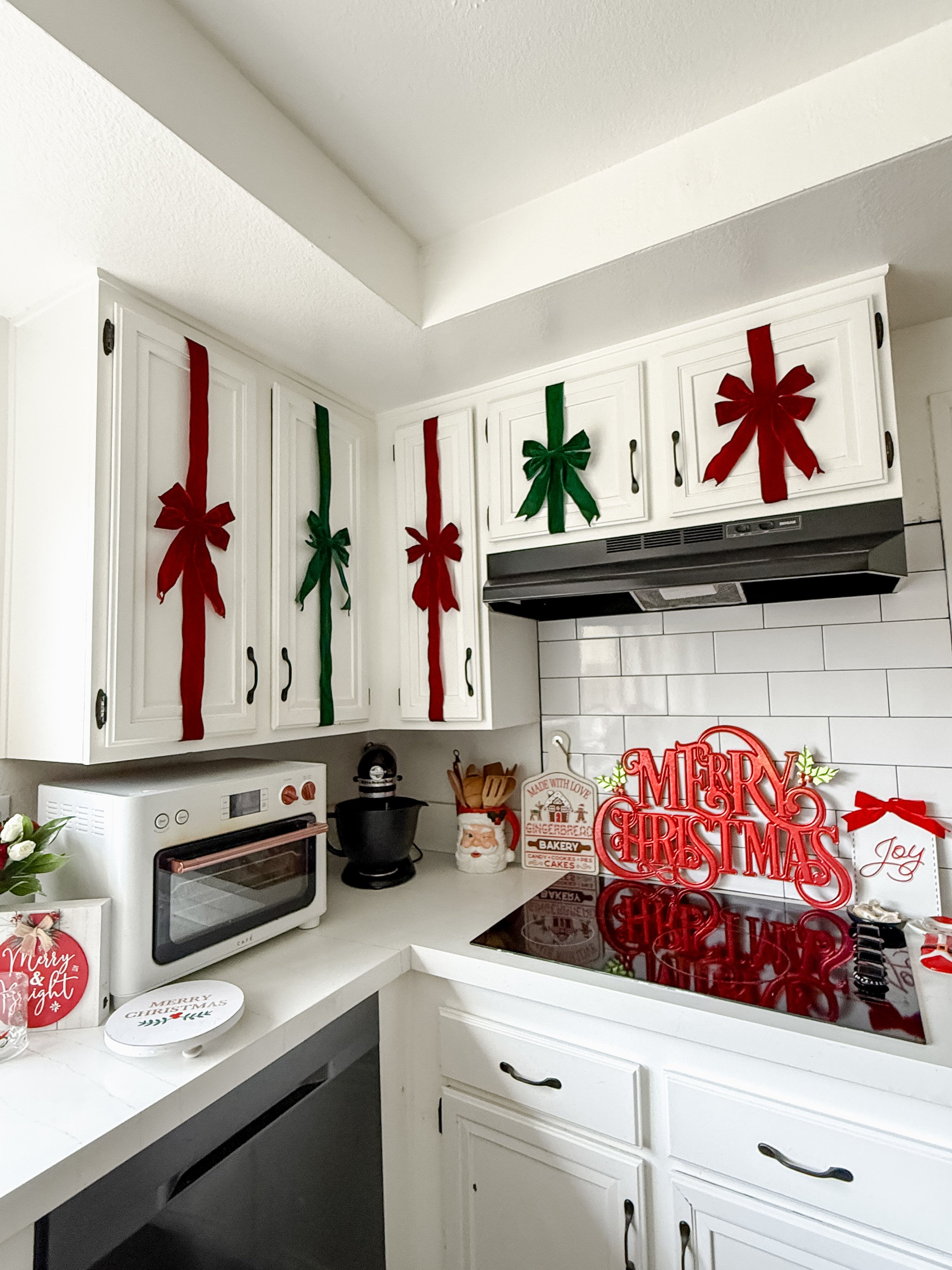 Kitchen decorated with red and green holiday bows on cabinets, a 'Merry Christmas' sign on the counter, and Christmas-themed decorations including a small 'Merry & Bright' sign and a 'Joy' card.