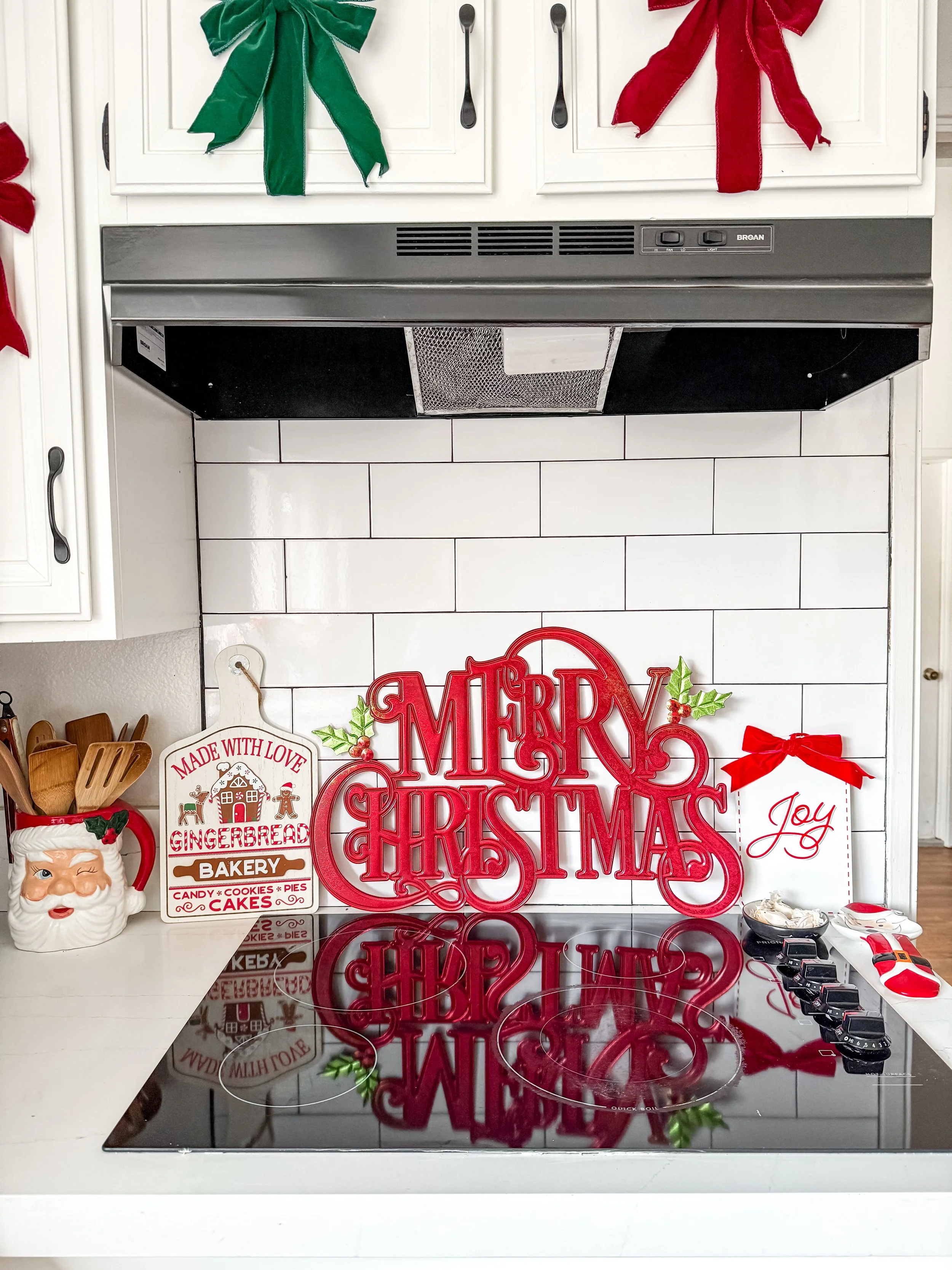 Christmas decorations on a kitchen stove, featuring a red "Merry Christmas" sign, a white 