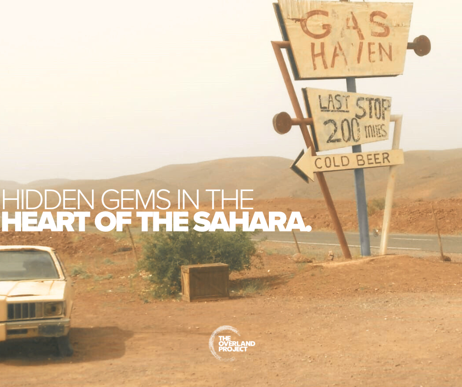 A desert road in the Sahara with a sign that says 'Gas Haven,' 'Last Stop 200 miles,' and 'Cold Beer.'