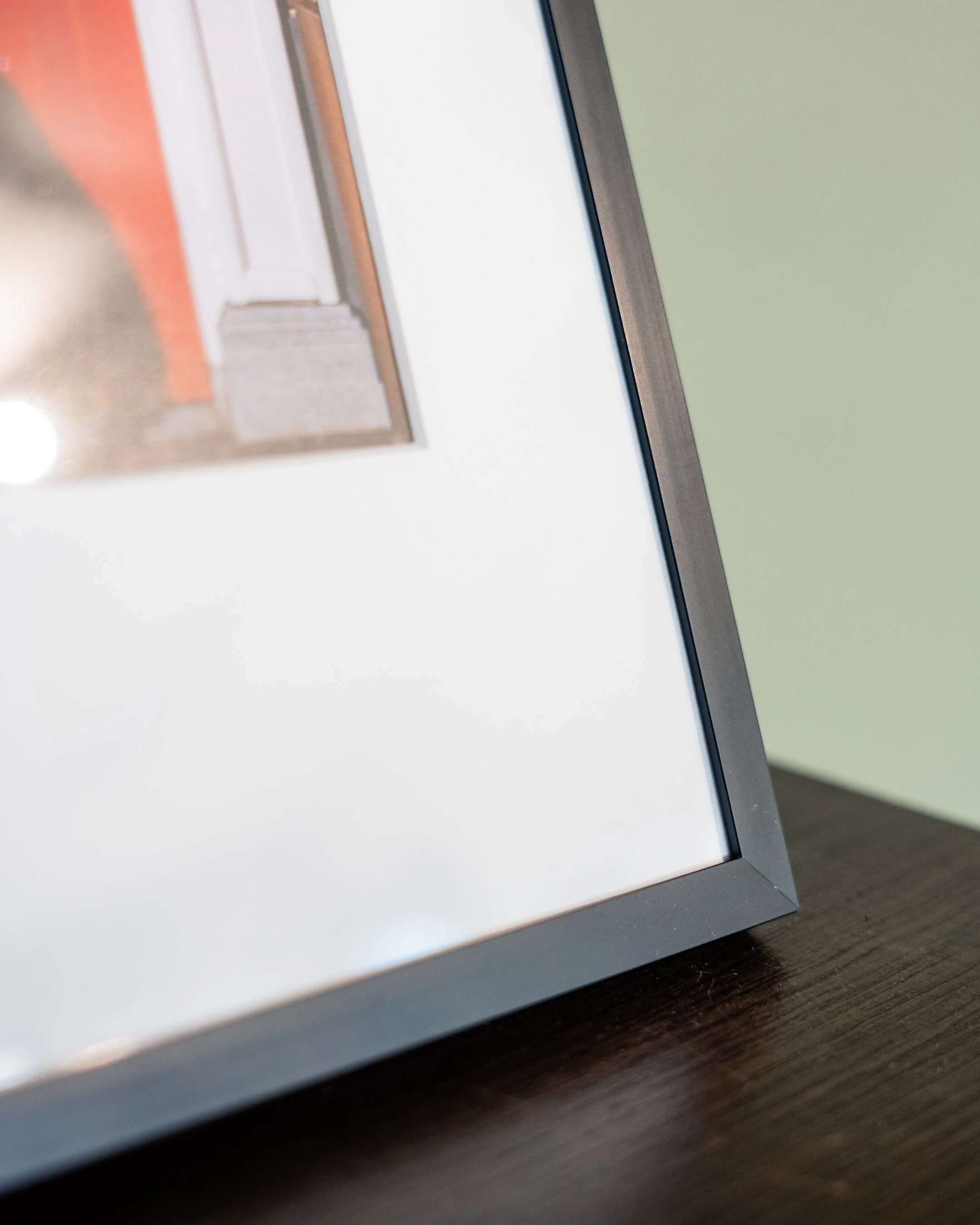 Close-up van een ingelijste foto op een houten oppervlak. De focus ligt op de metalen lijst en een deel van de foto is zichtbaar met wat lijkt op delen van een deurpost in de achtergrond.