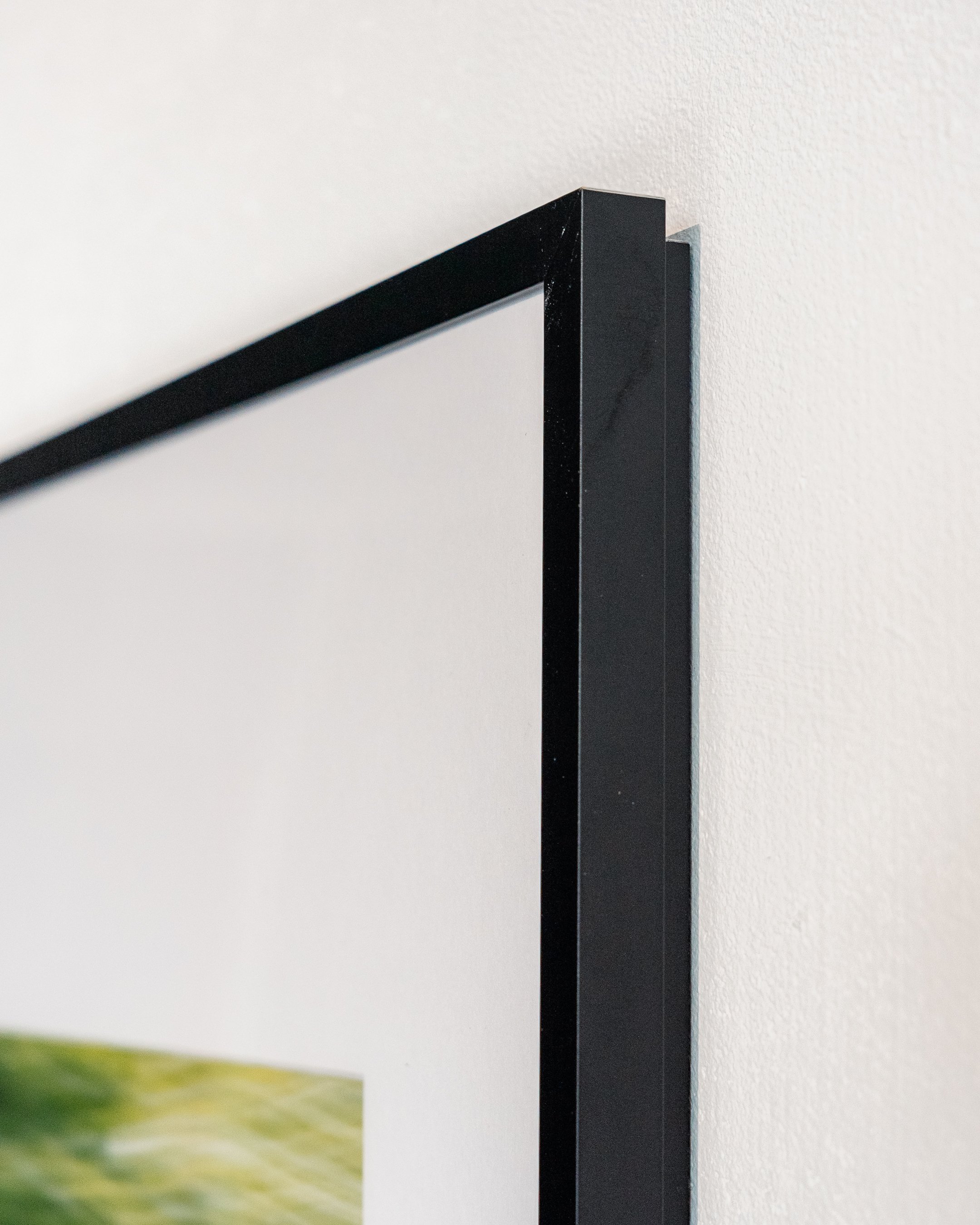Zijaanzicht van een zwarte fotolijst aan de muur met een deels zichtbaar kunstwerk.