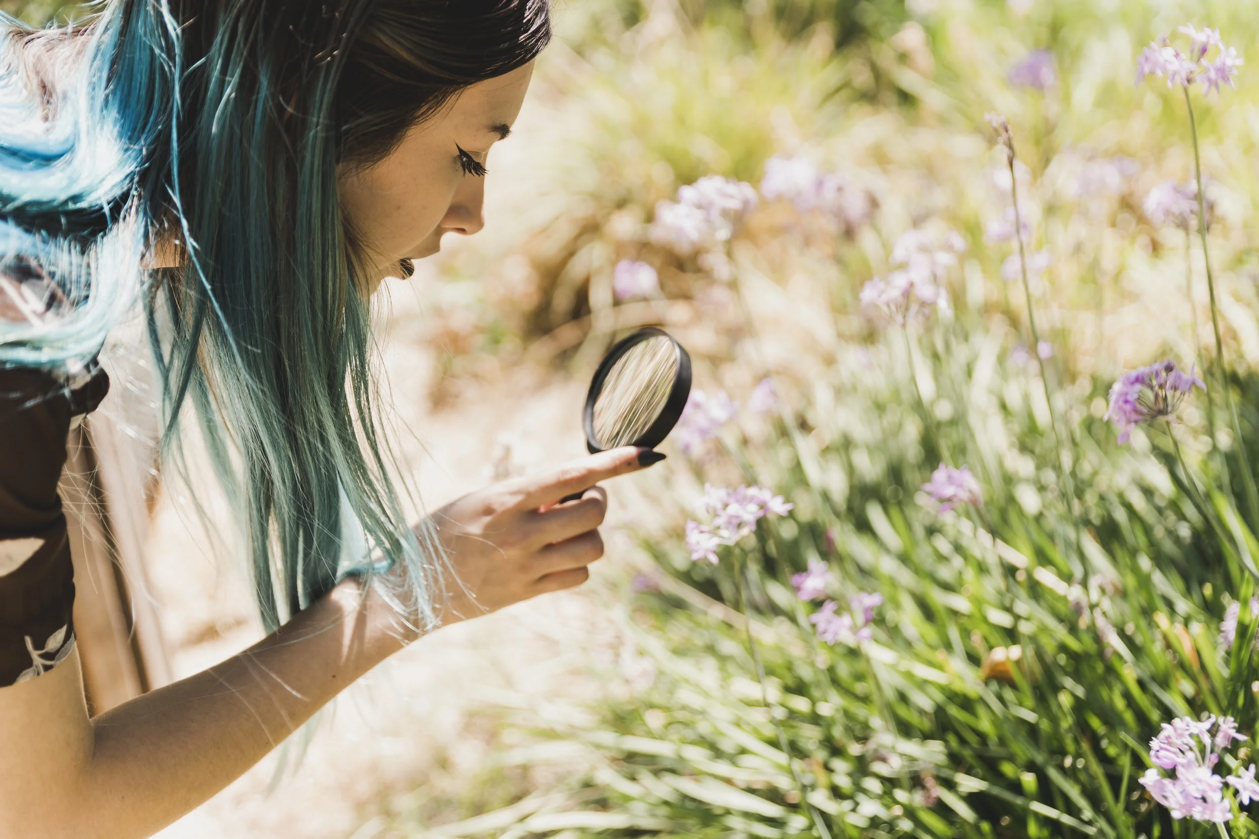 Jeune femme observant des fleurs à l'aide d'une loupe dans un jardin en plein air.