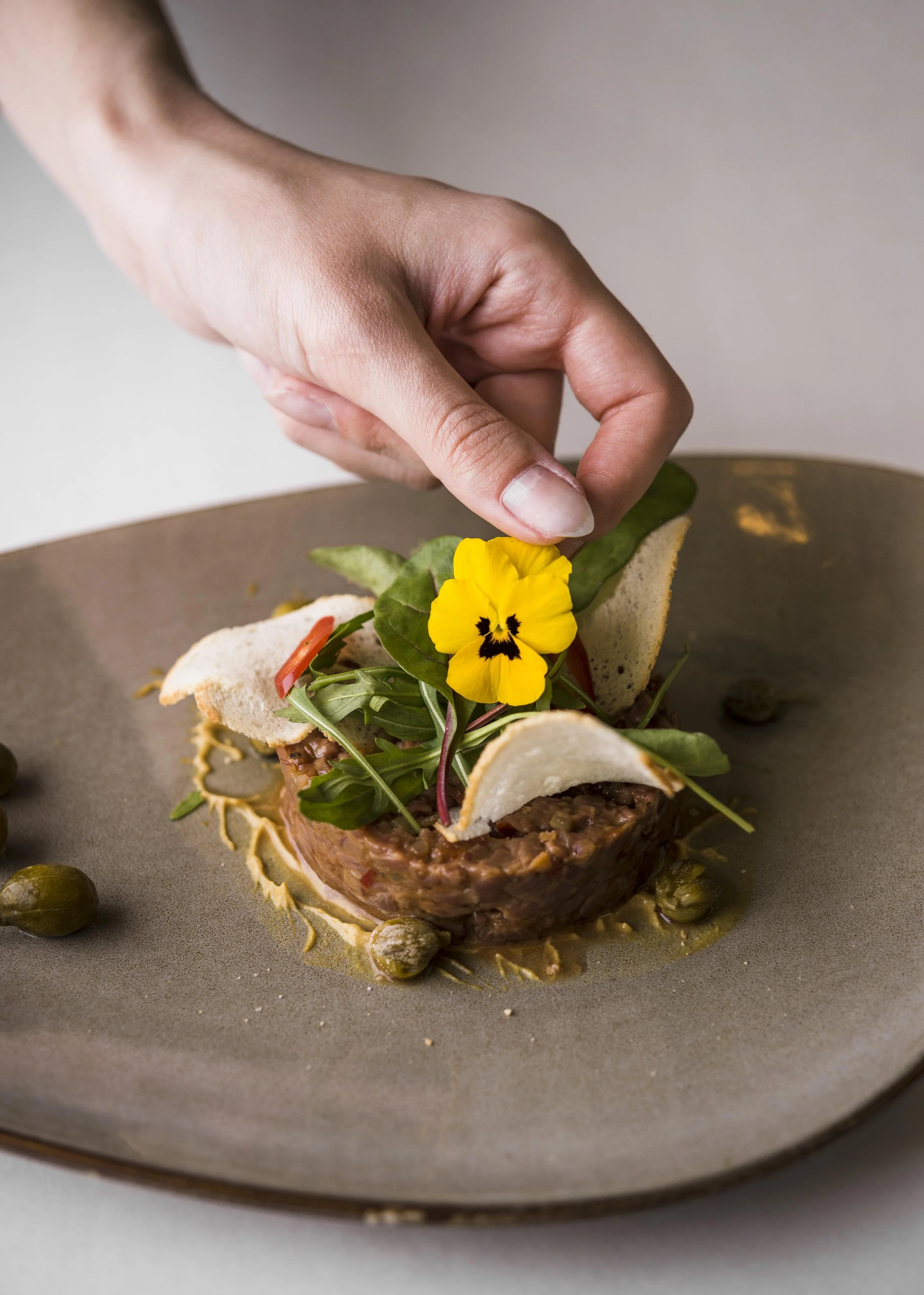 Une main décore un plat gastronomique avec une petite fleur jaune.
