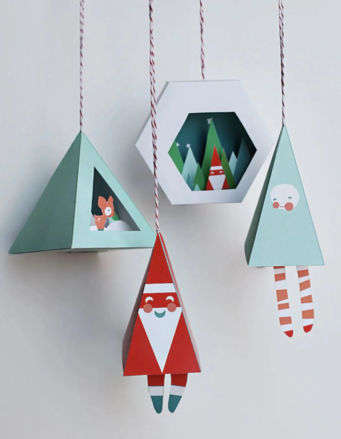 Paper Christmas decorations featuring Santa Claus, an elf, a reindeer, and trees, hanging from red and white string. Author-Illustrator Mari Richards picture book illustration and art full of monsters, animals, quirky kids.