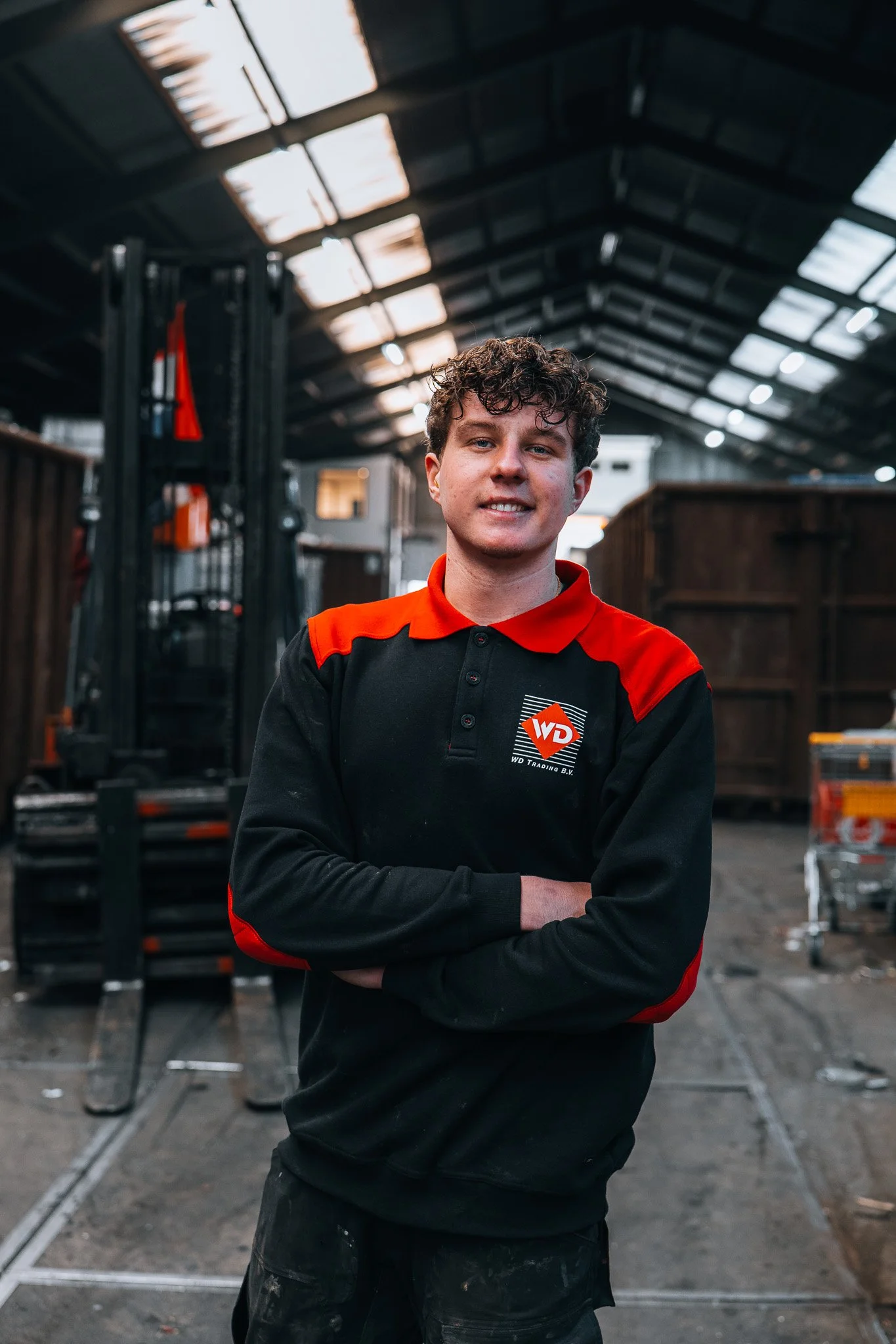 Man in een zwart en rode werkkleding met het logo 'WD Trading' op de borst, staand met armen over elkaar in de loods van WD in Krimpen aan den IJssel