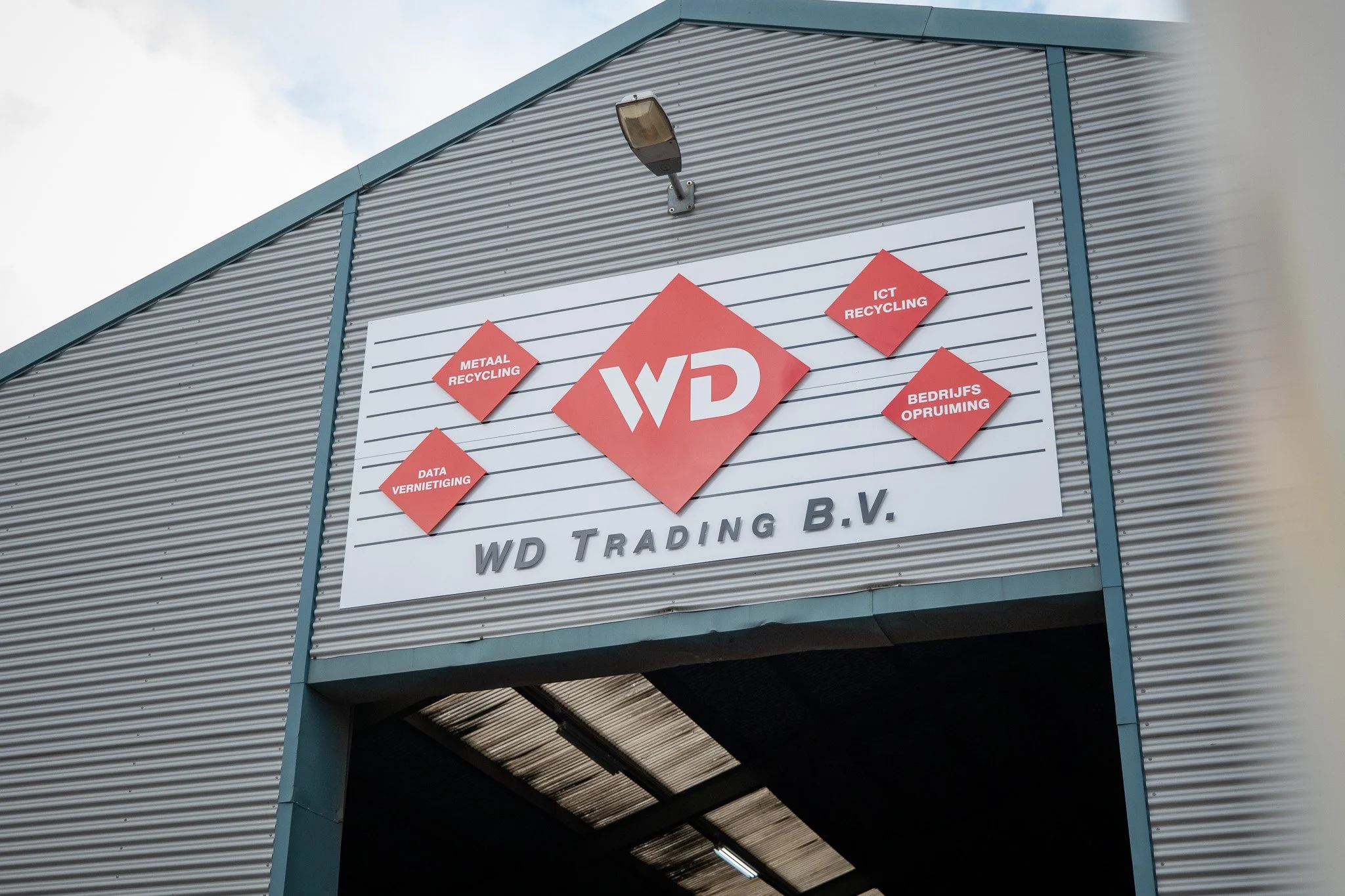 Buitengevel met bedrijfssignage van WD Trading B.V., inclusief logo en diensten zoals metaal recycling, ICT recycling, data vernietiging en bedrijfsopruiming, op een gebouw met metalen gevel.