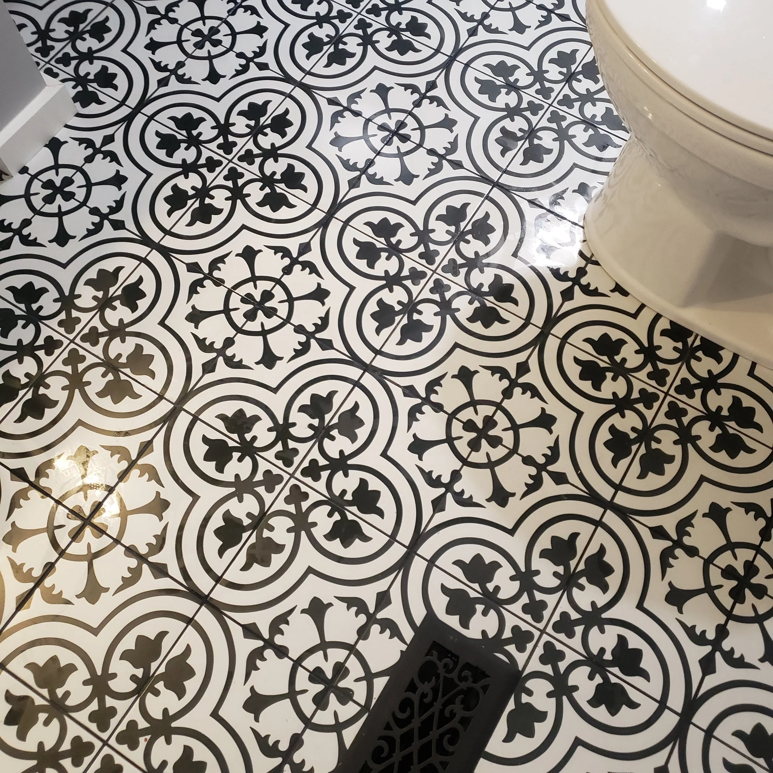 Black and white patterned tile floor in a bathroom with a toilet and a floor drain.