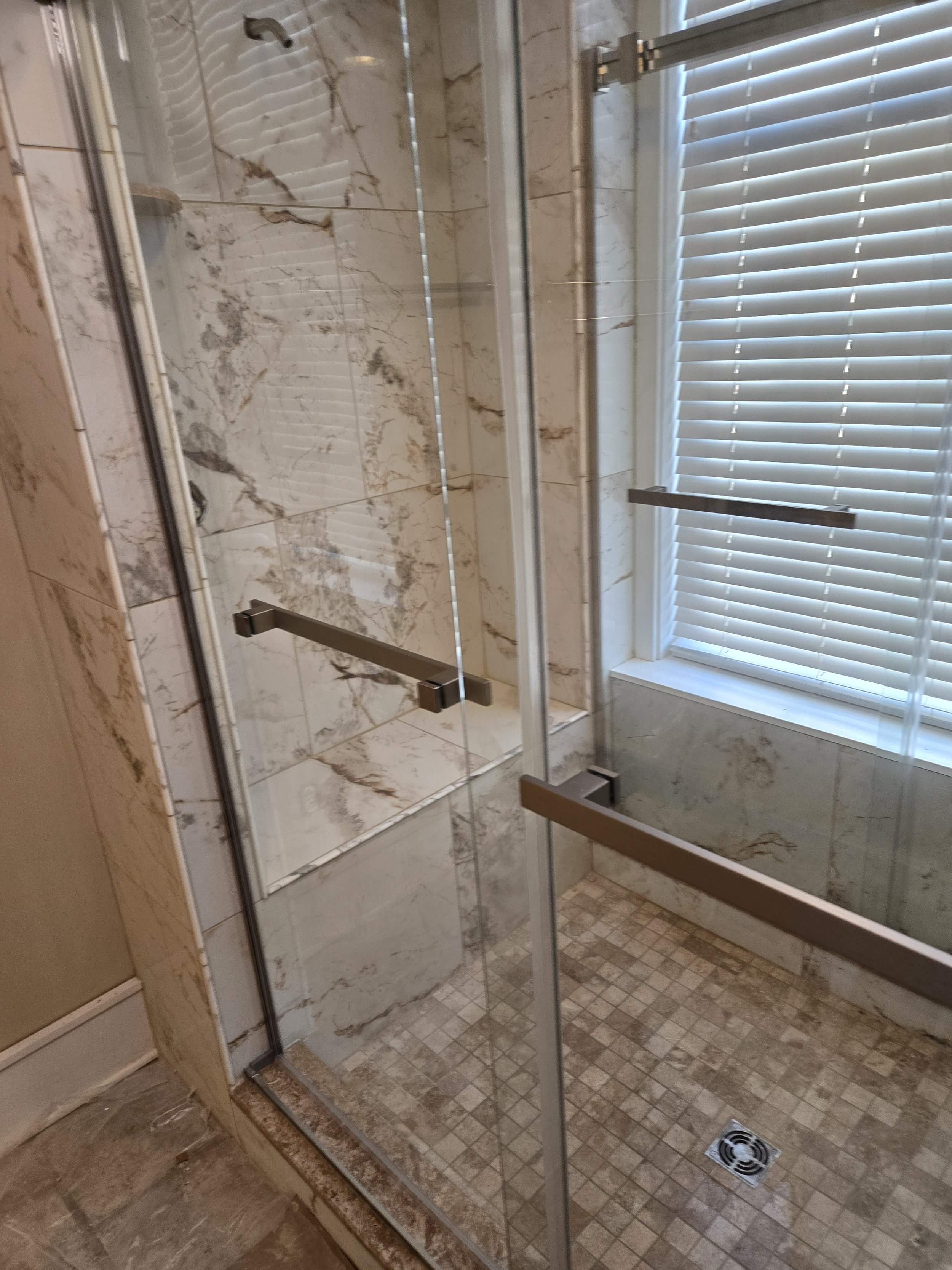 Walk in shower with sliding glass doors and tan marbled tile