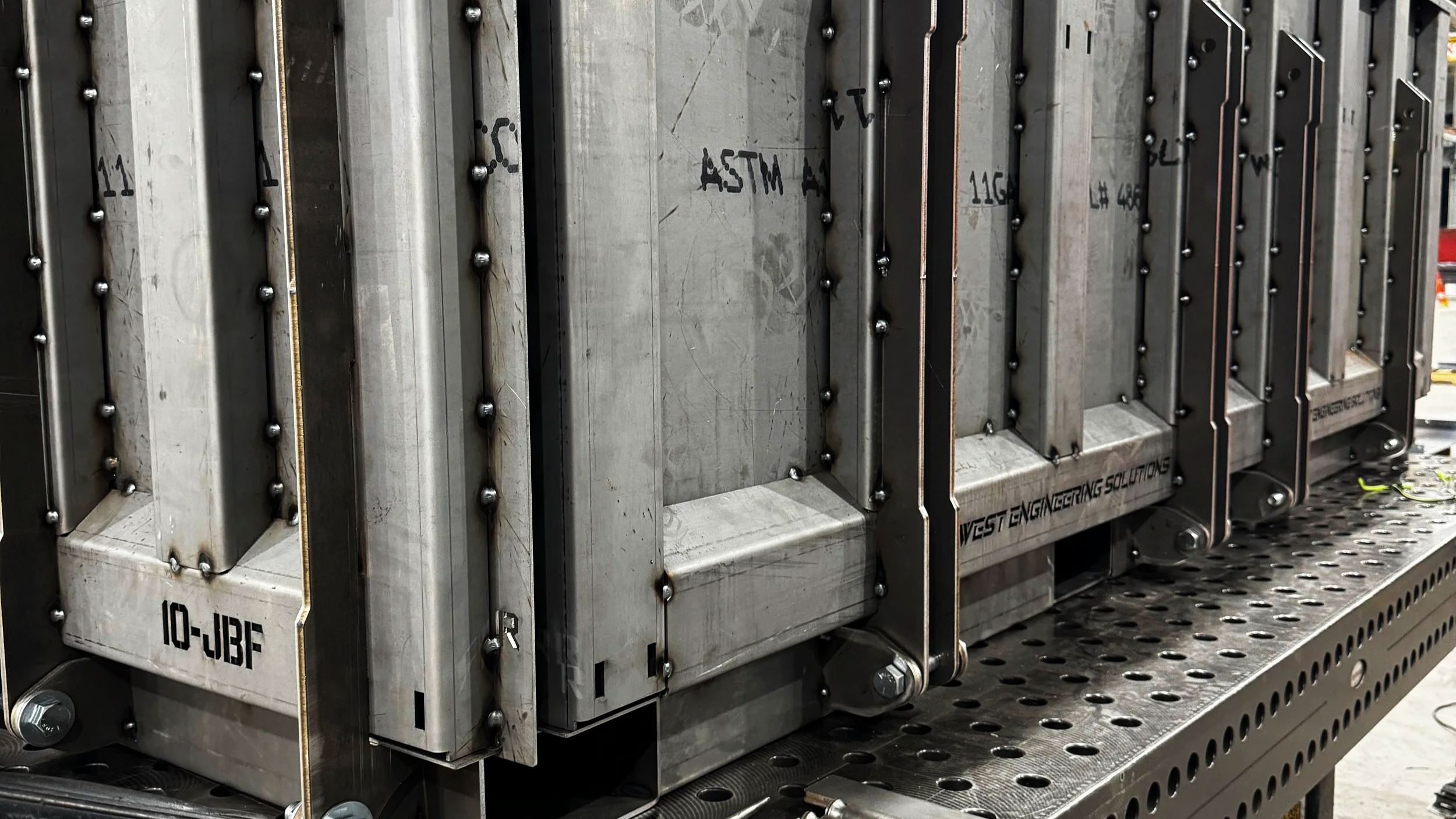 Close-up view of industrial machine parts with metallic panels, bolts, and labels, mounted on a perforated metal surface.