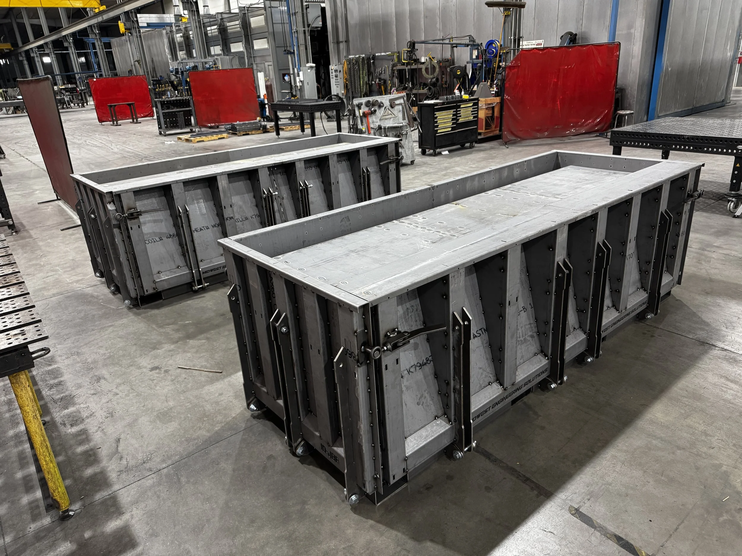 Industrial workshop with metal molds, tool cabinets, red safety barriers, and manufacturing equipment.