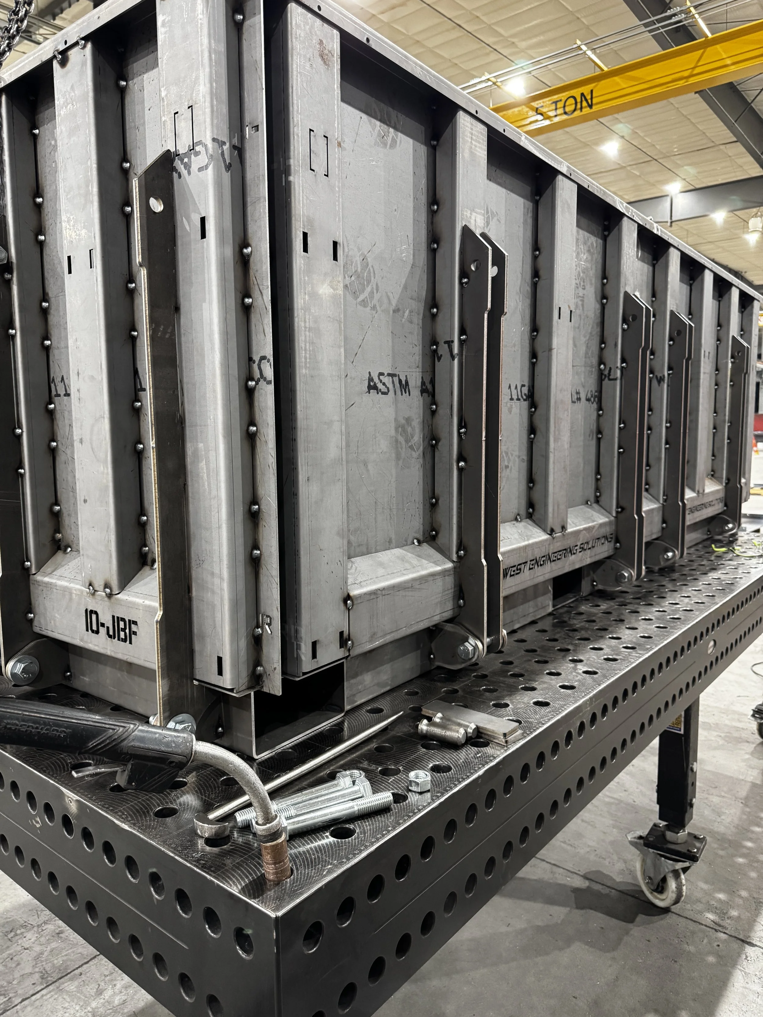 Metal industrial equipment with pipes, bolts, and structural components on a workbench in a factory setting.