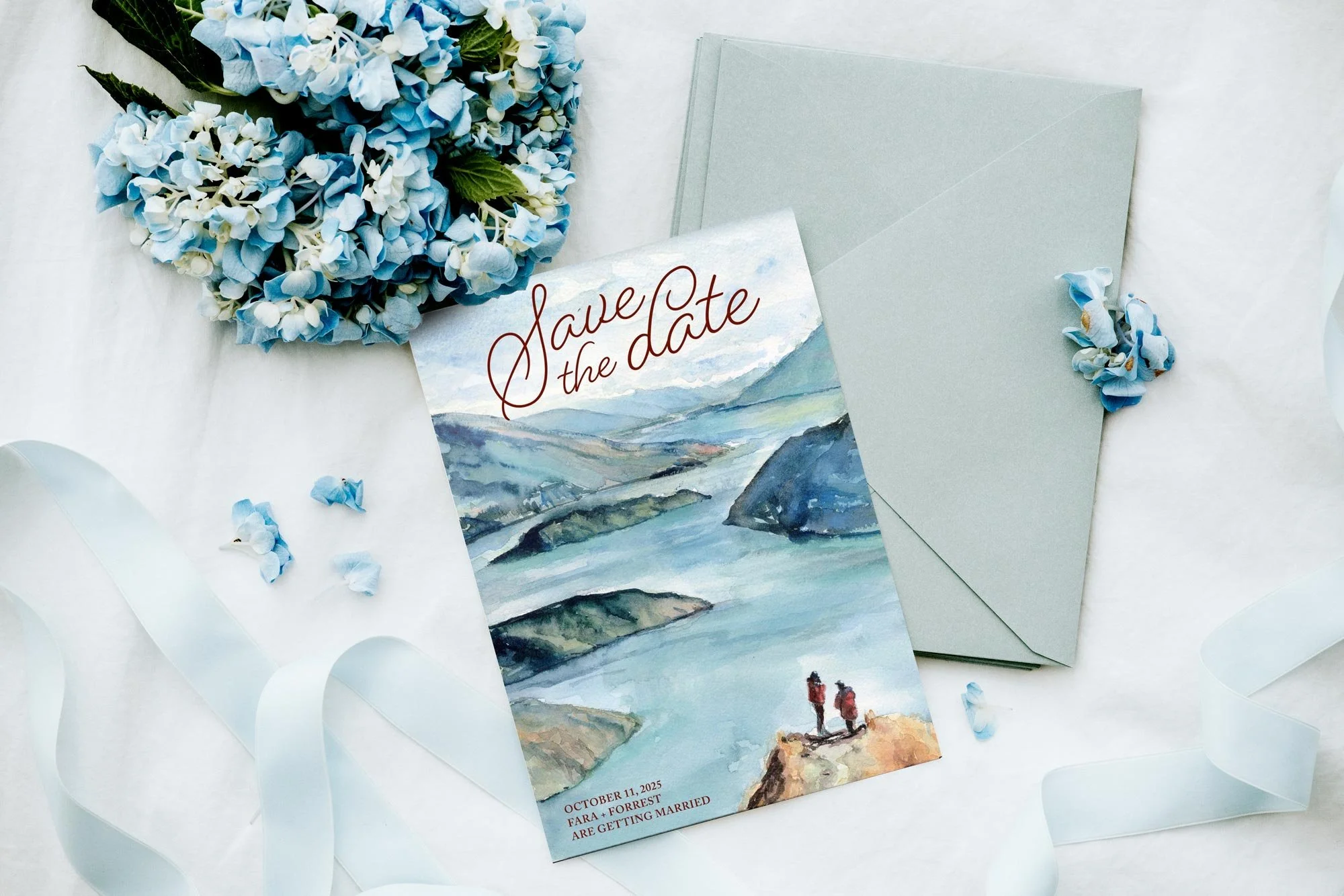 A watercolor style save the date card with a landscape view of mountains and water, featuring two people standing on a rocky outcrop, and text indicating the date October 11, 2025, and the names of the couple, Fara and Forrest, getting married. The c